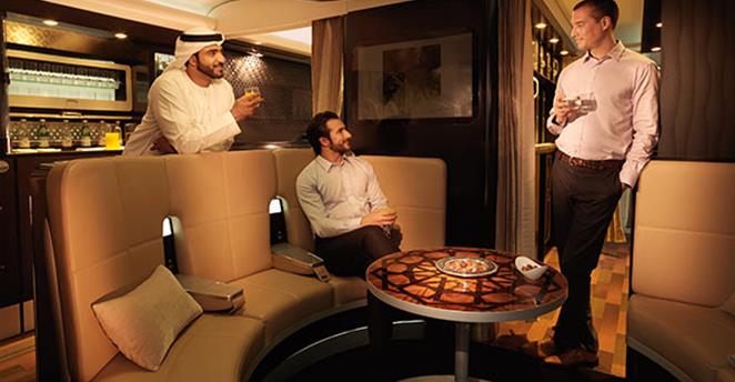 Three men socialize and enjoy drinks in a luxurious airplane cabin with a bar and lounge seating.