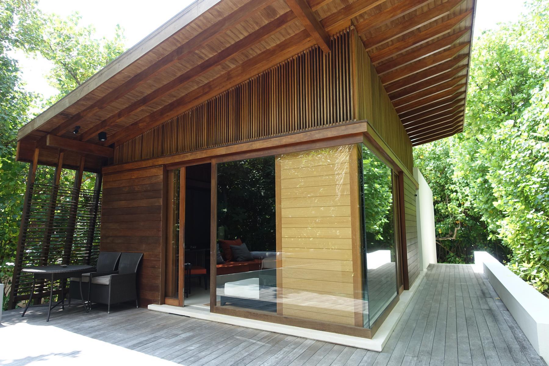 Modern wooden villa with a deck, large glass windows, and a sloping roof, surrounded by green trees.