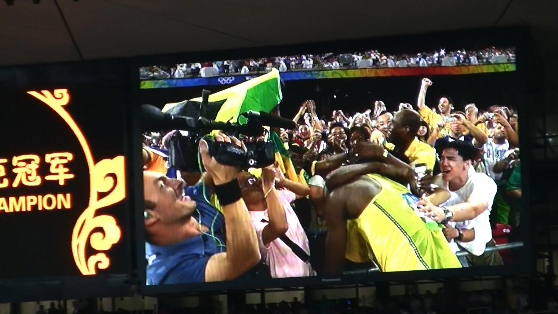 A stadium jumbotron shows Usain Bolt celebrating his win with fans and media after the Beijing 2008 Olympic 100m final.