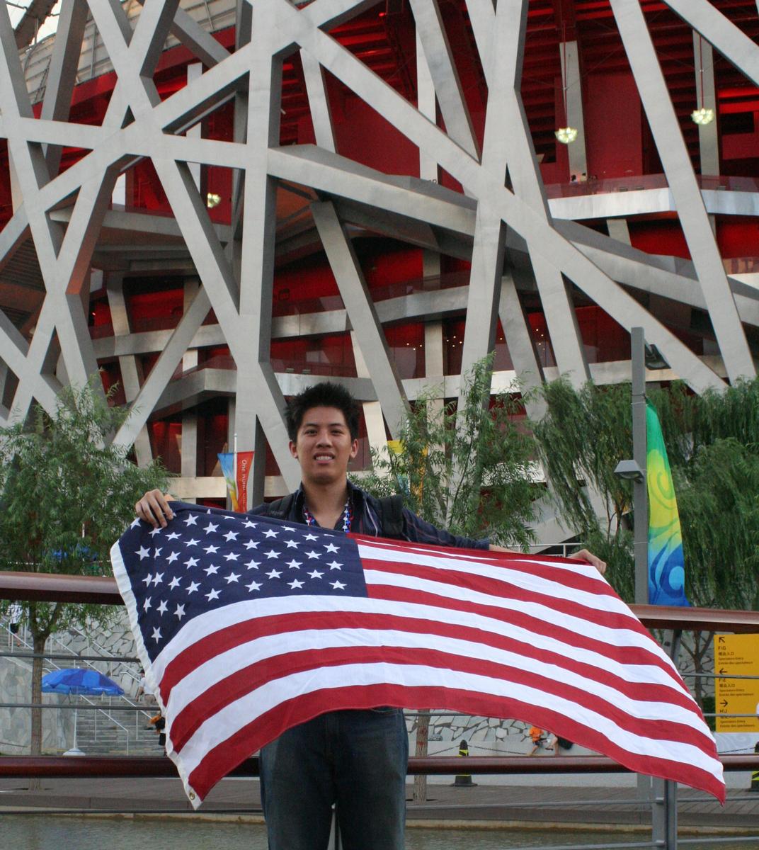 A young person holds an American flag in front of the Beijing National Stadium.