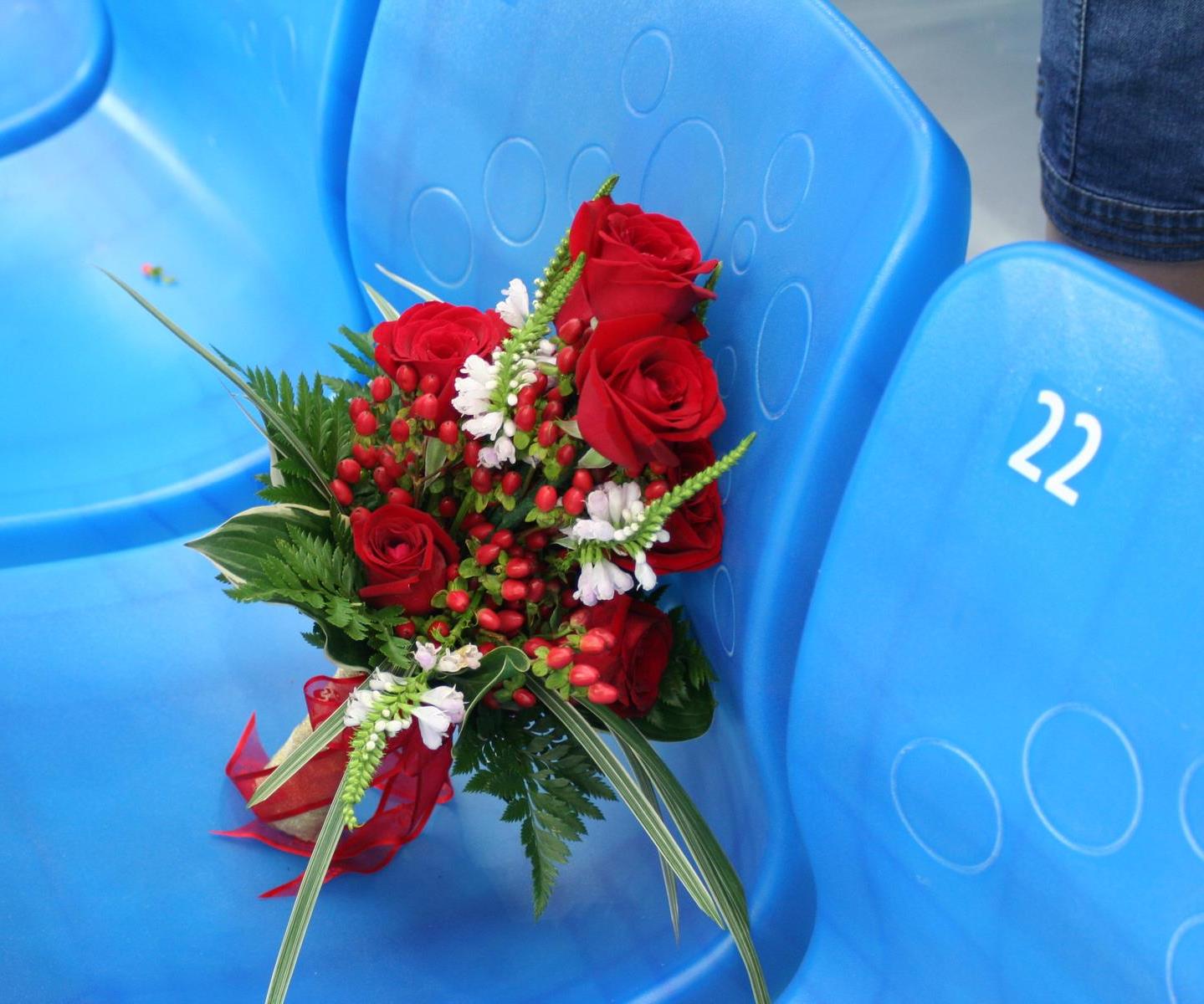 A bouquet of red roses and berries rests on blue stadium seats, with seat number 22 visible.