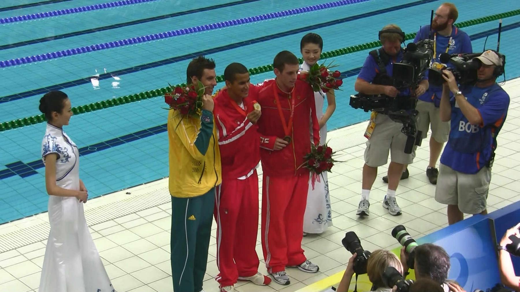 Michael Phelps and other Olympic swimmers pose with their medals and flowers by the pool as photographers capture the moment.
