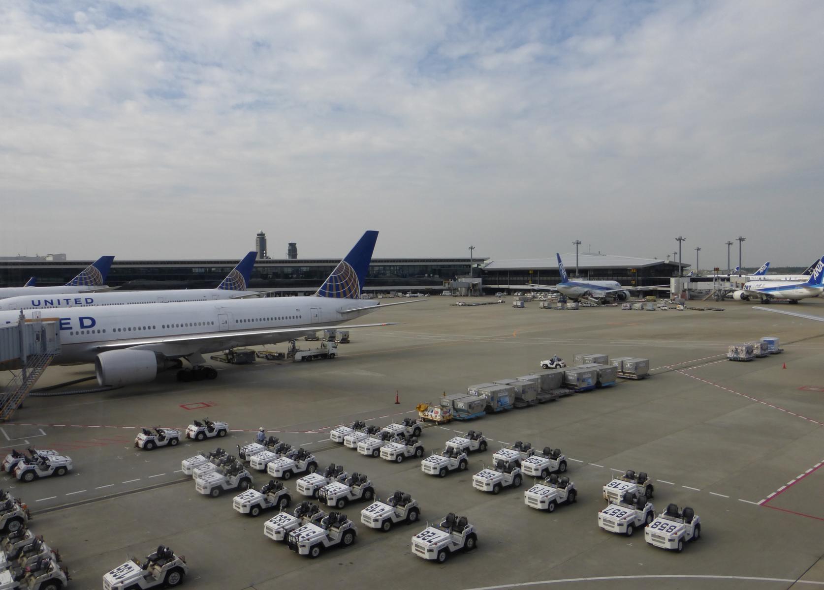 View from an airport lounge window showing multiple United and ANA aircraft, ground vehicles, and airport terminals in Tokyo.