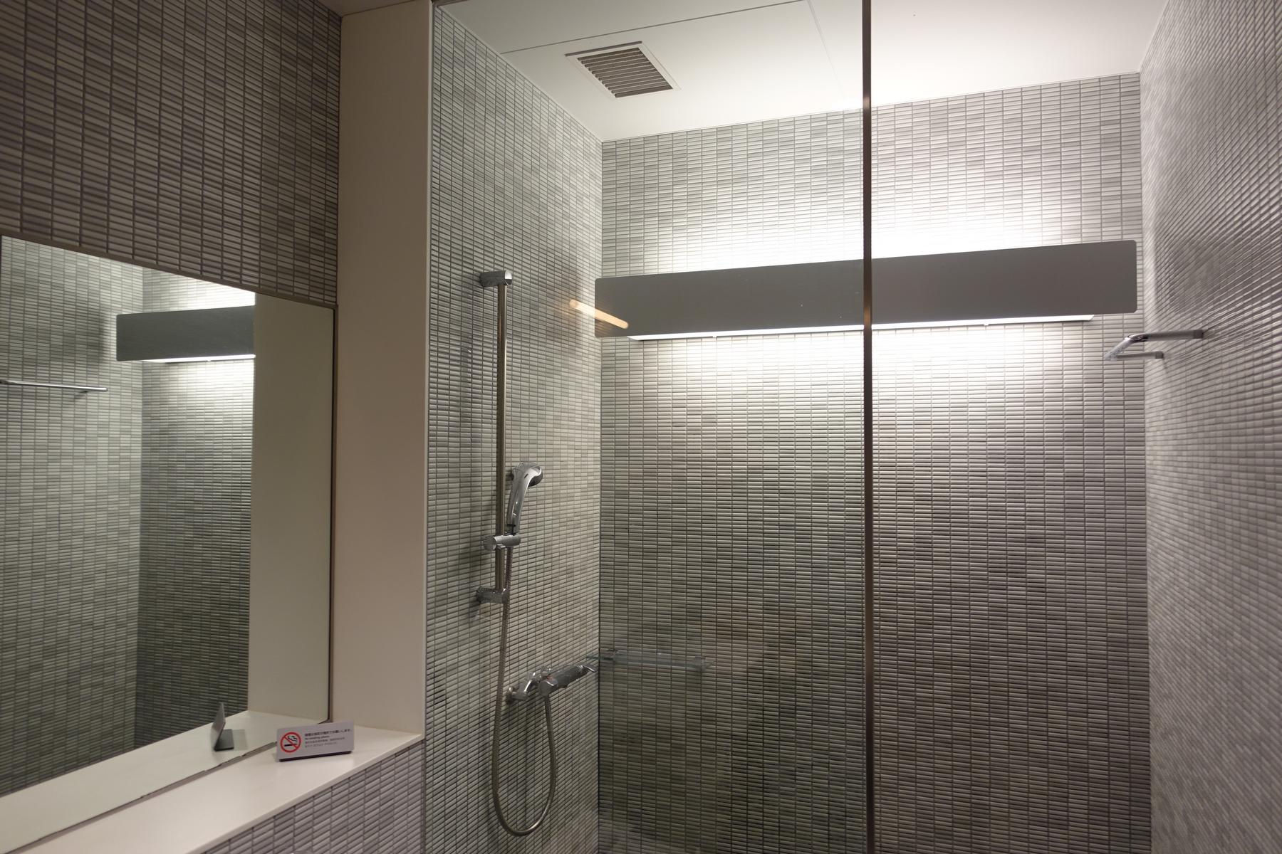 A sleek, modern shower room featuring gray mosaic tile walls, a glass partition, and a mirror.