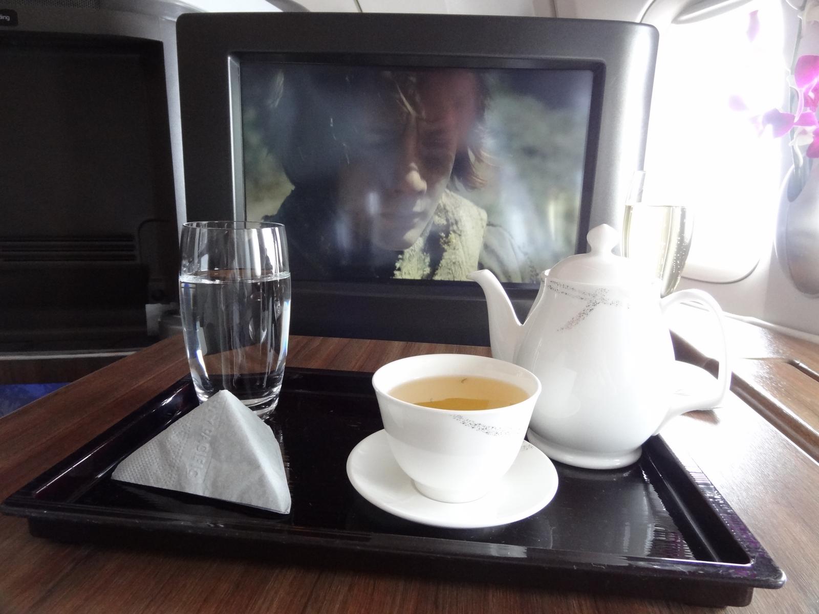 Tea and water on a tray in Cathay Pacific First Class, with a movie playing on the in-flight screen.