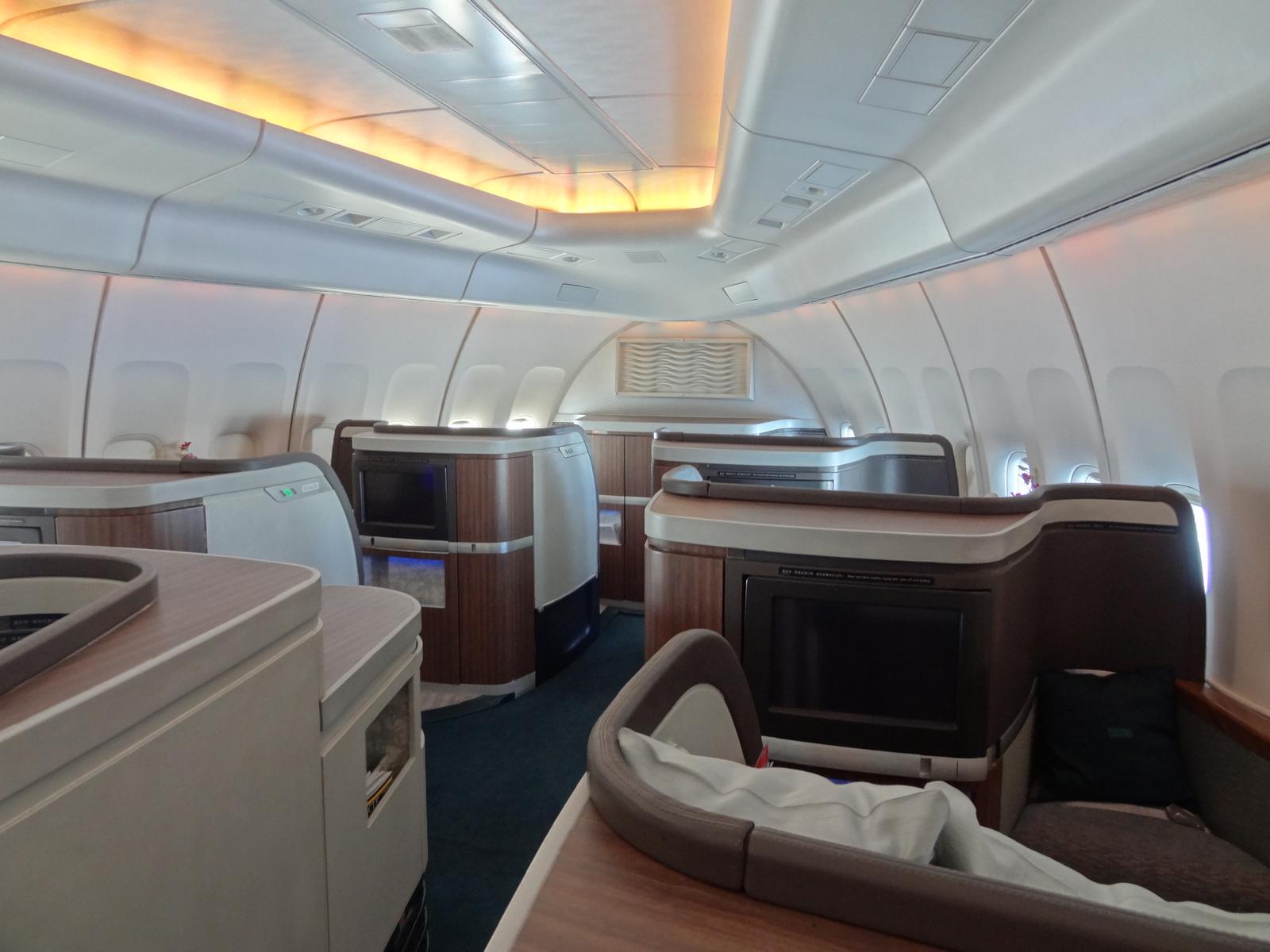 Interior of a Cathay Pacific 747 First Class cabin with spacious private suites, screens, and warm ambient lighting.