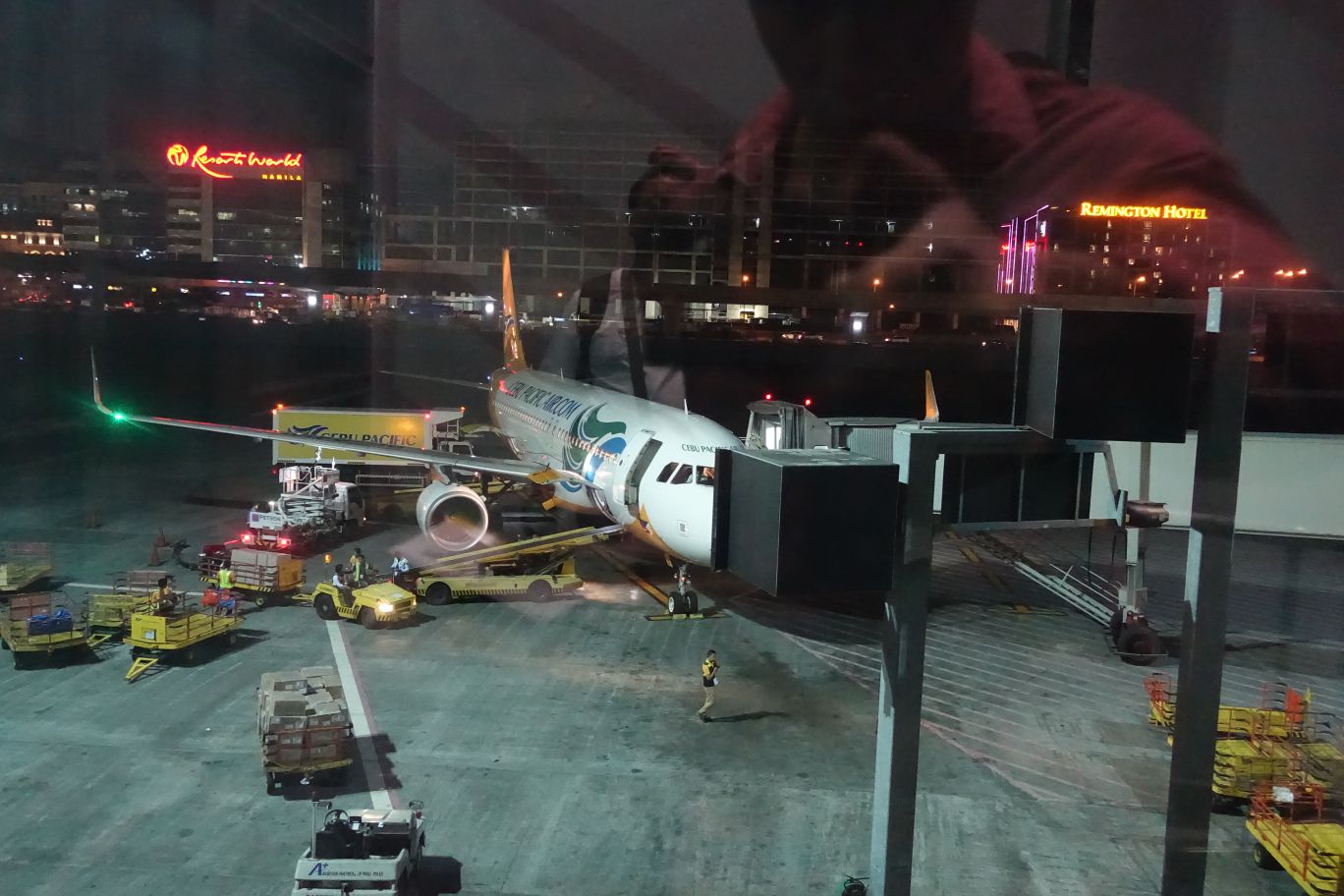 Cebu Pacific aircraft parked at a Manila airport gate at night, with ground crew preparing the aircraft.