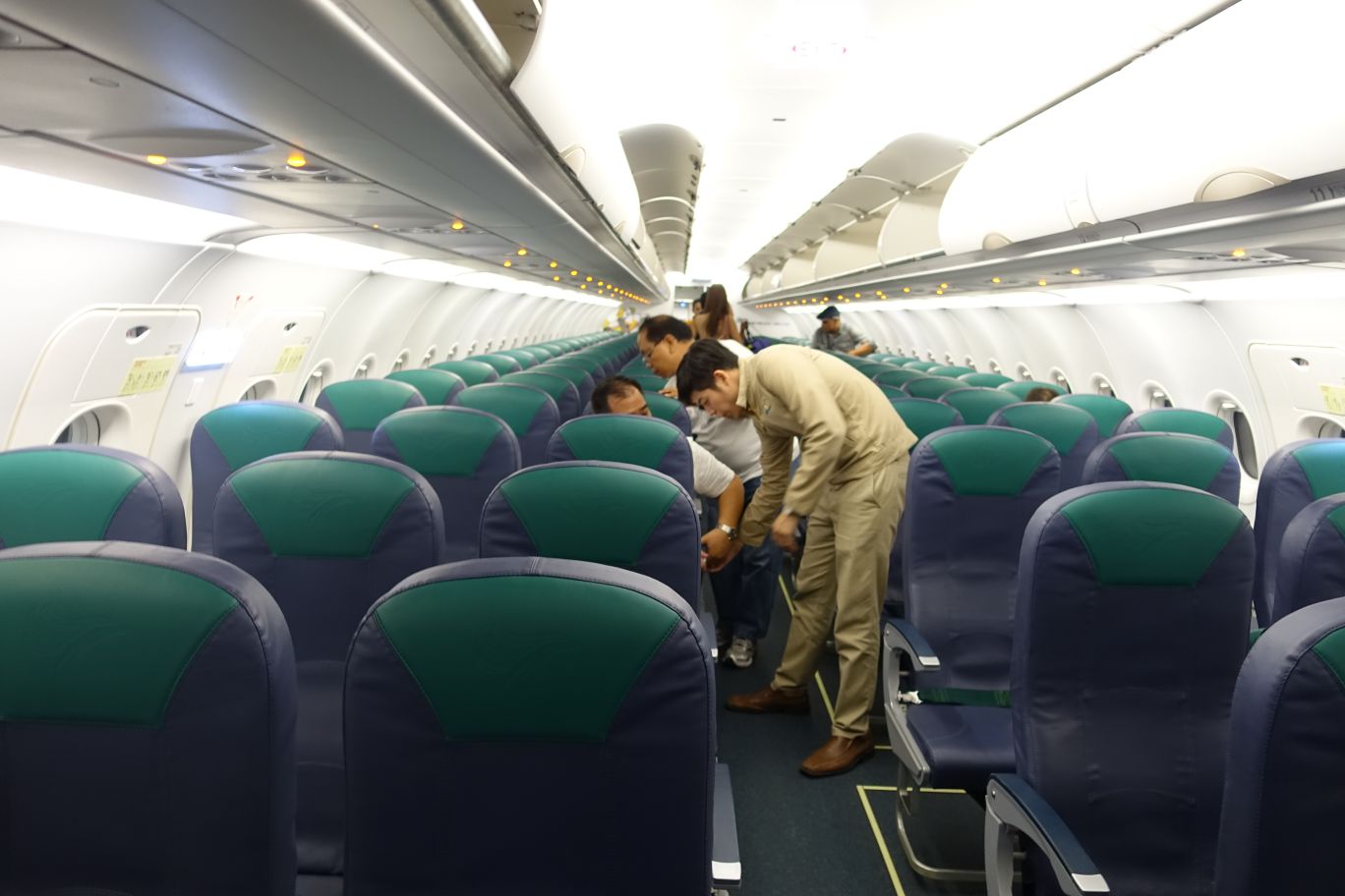 Interior of a Cebu Pacific economy class airplane cabin with blue and green seats and a few passengers.