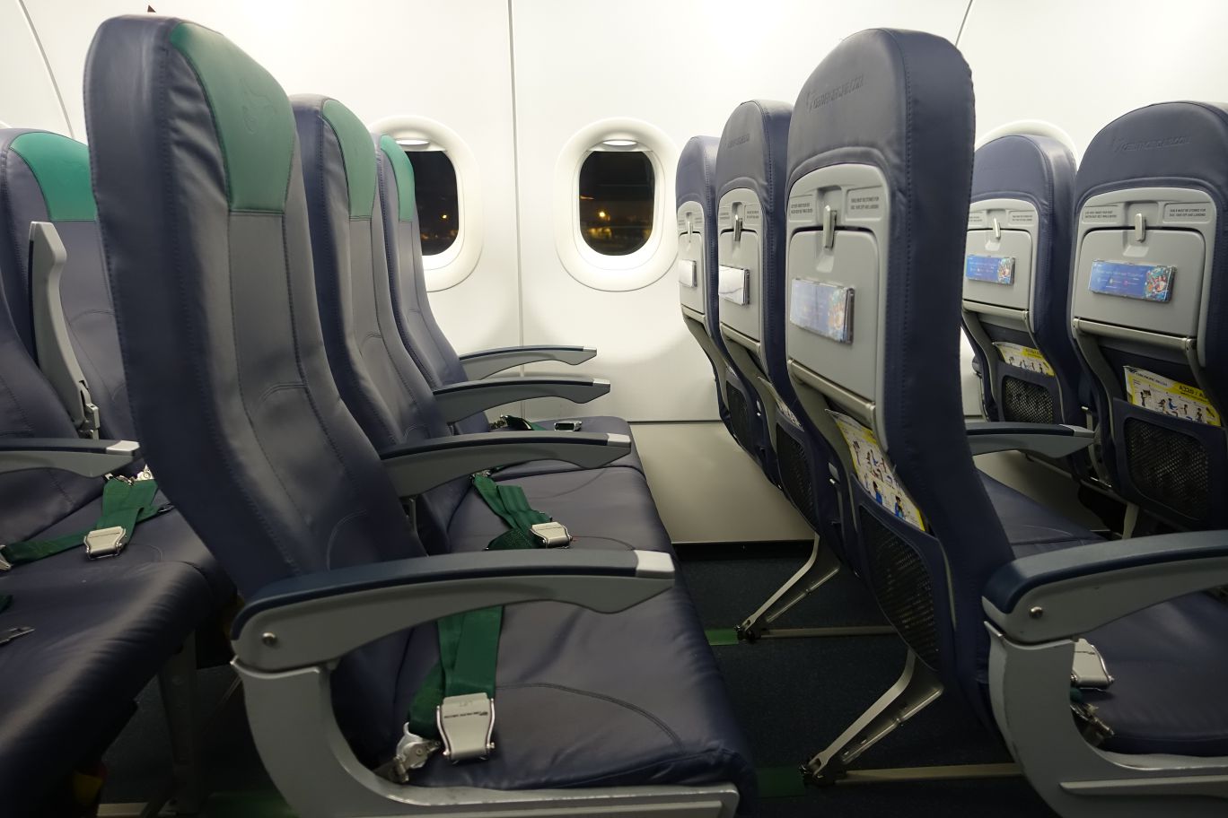 Cebu Pacific economy class airplane interior with empty blue and green seats and windows looking out into the night.