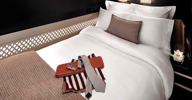 A luxurious Etihad First Class suite bed with white linens, a brown pillow, and a watch, tie, and leather case.