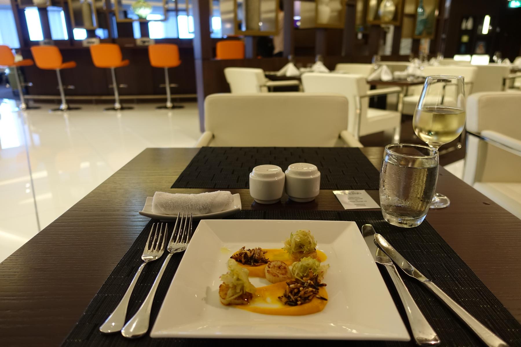 A meticulously plated dish of scallops, puree, and garnishes sits on a table in a luxurious dining area.