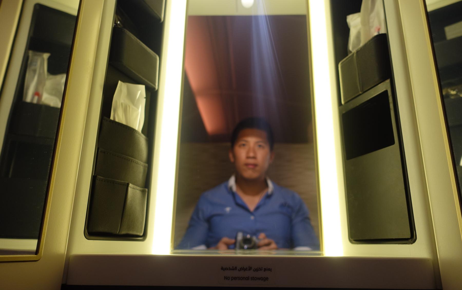 Reflection of a man holding a camera in a luxurious Etihad First Class cabin.