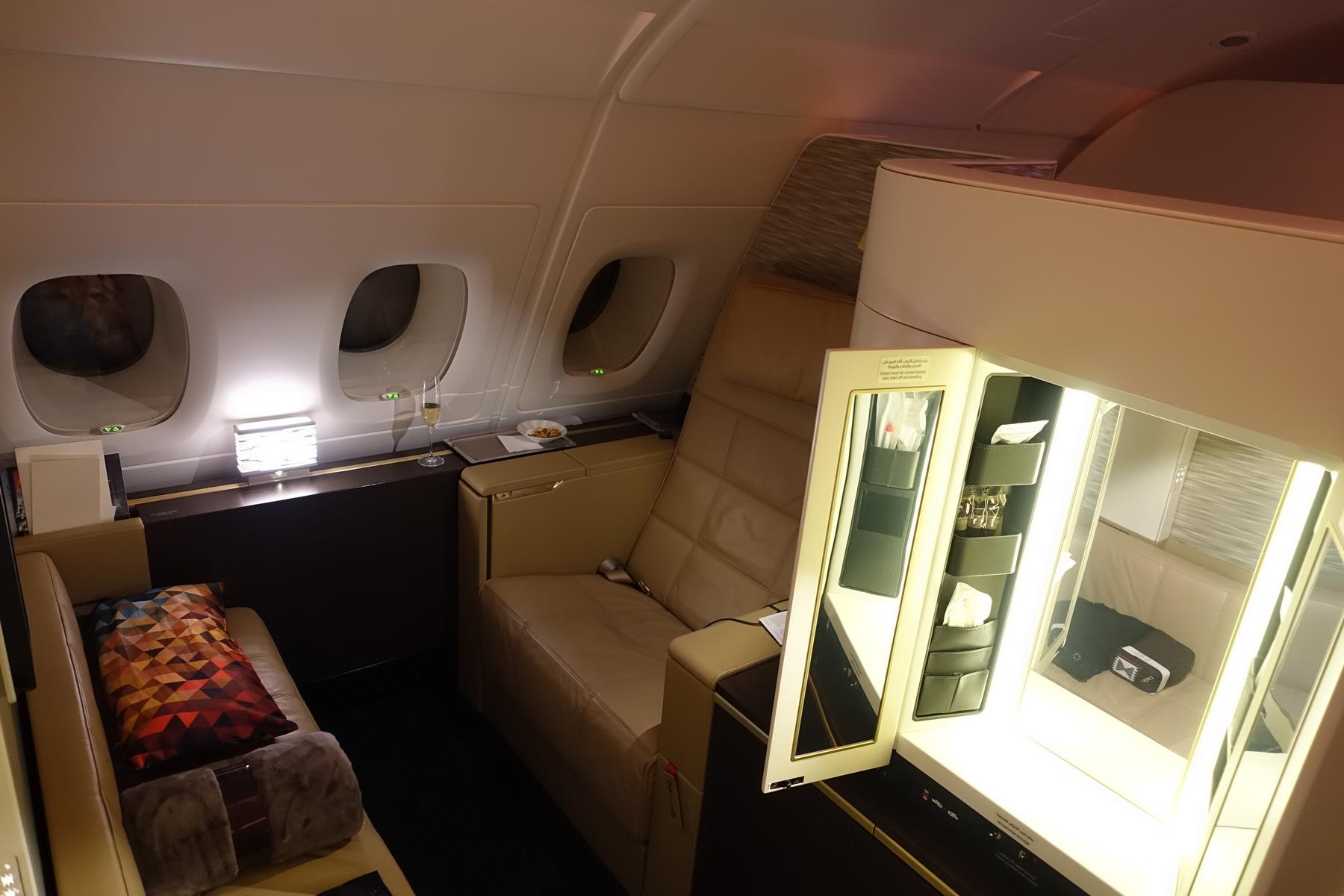 A luxurious Etihad A380 First Class 'Apartment' suite with a beige couch, armchair, and illuminated vanity.