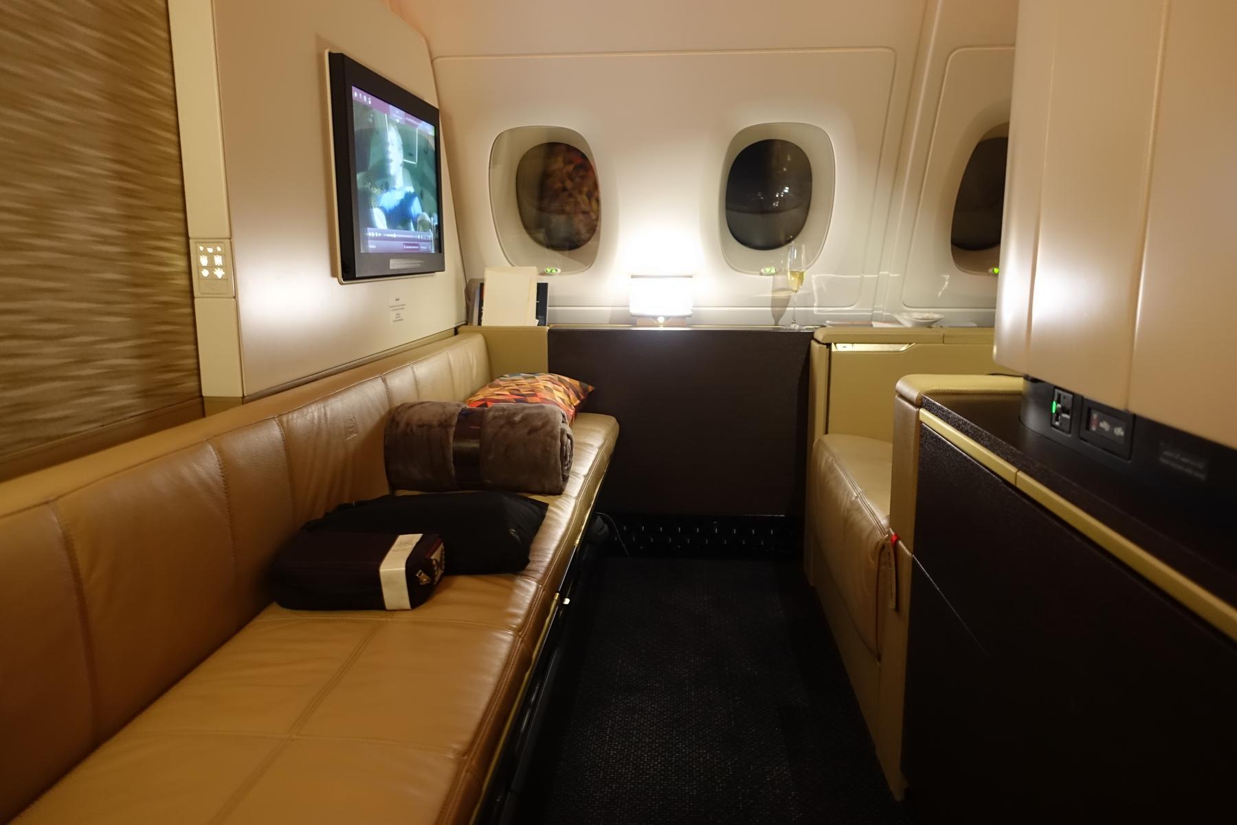 Luxurious Etihad A380 First Class suite featuring a tan leather sofa, large TV, and windows.