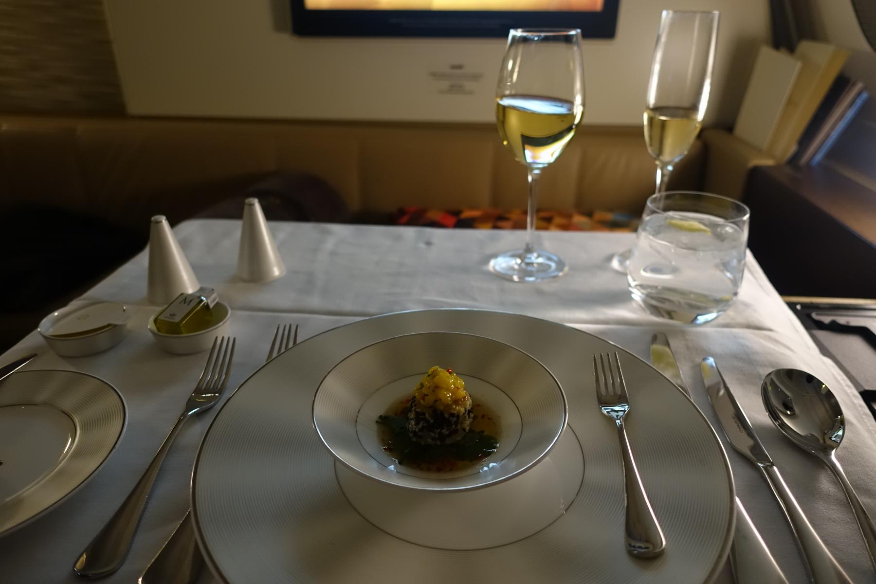 A beautifully set table with a gourmet dish, wine, and water in an Etihad first class cabin.
