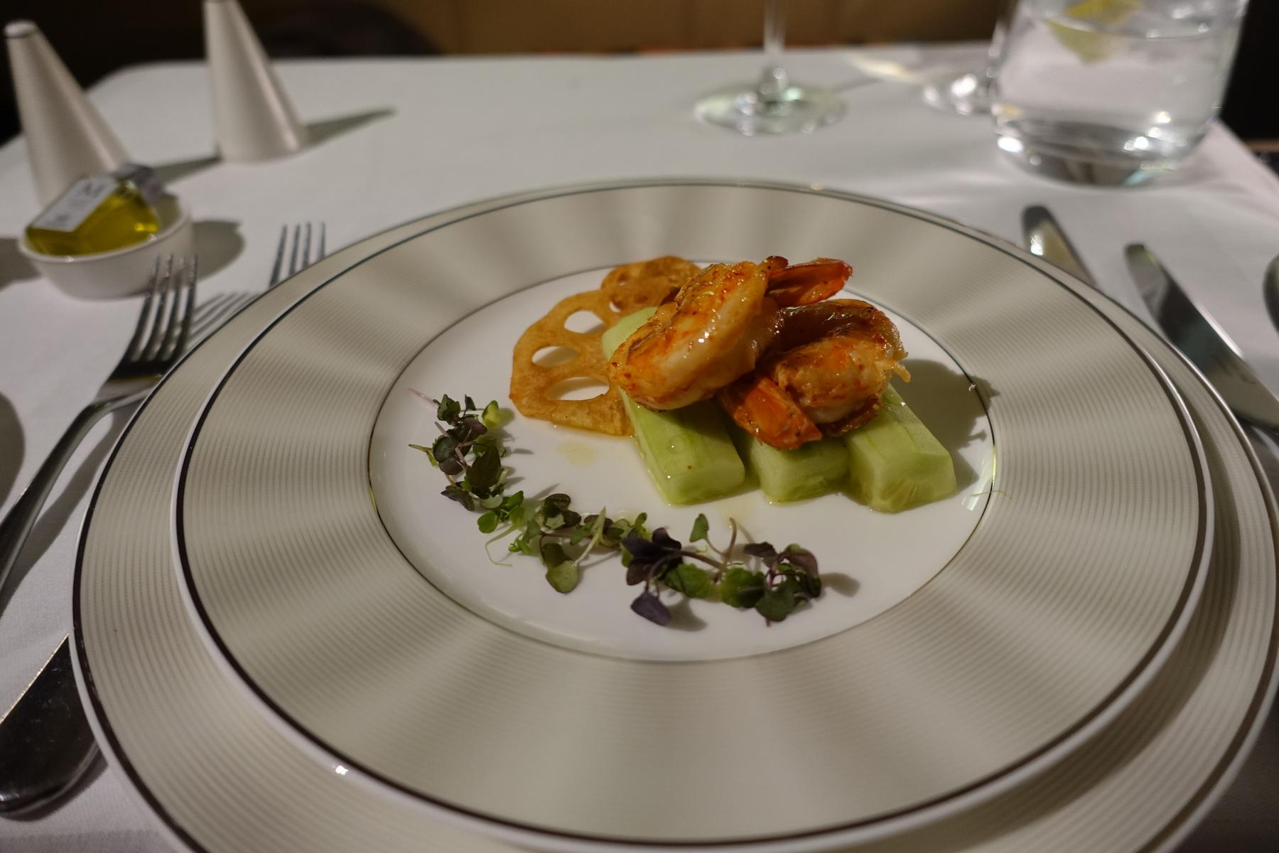 Gourmet shrimp with cucumber, lotus root, and microgreens is beautifully plated on elegant airline china.