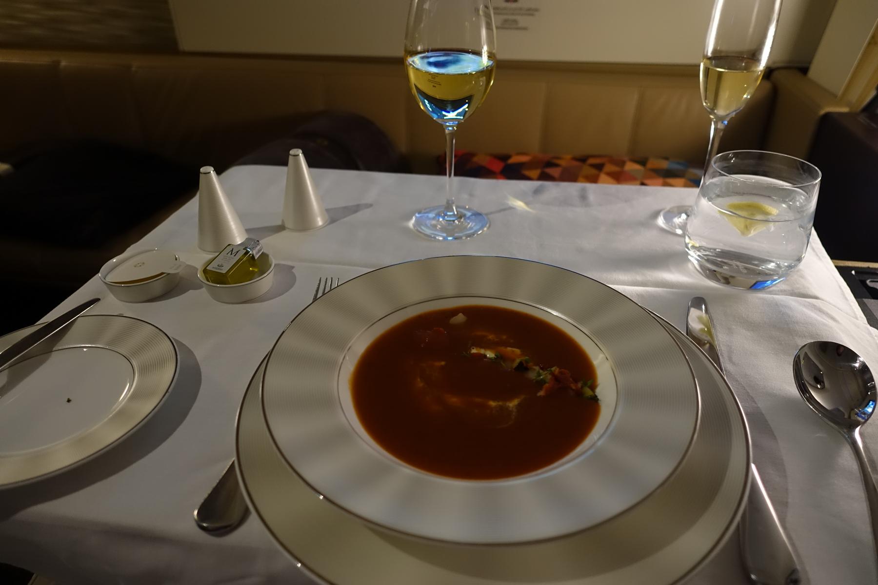 A meticulously set dining table in an airplane's first class, featuring soup, drinks, and condiments.