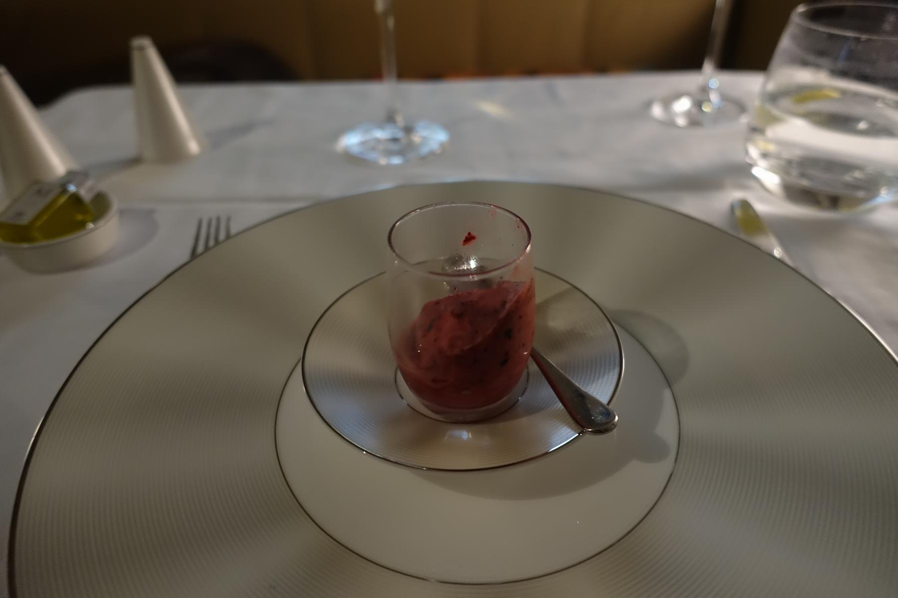 A red sorbet dessert in a glass on elegant plates, served in an airline first-class cabin.