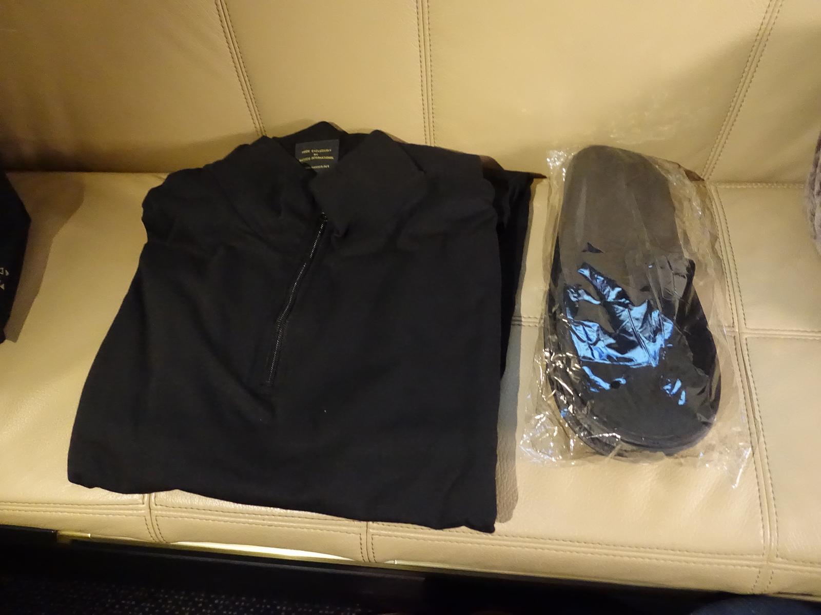 Etihad-branded black sleepwear and packaged slippers are laid on a cream leather seat.