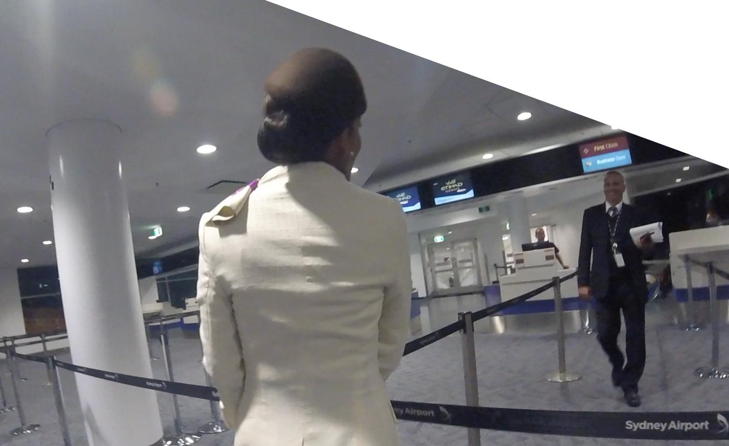 A person walks through the Etihad check-in area at Sydney Airport, with a smiling airline staff member approaching.
