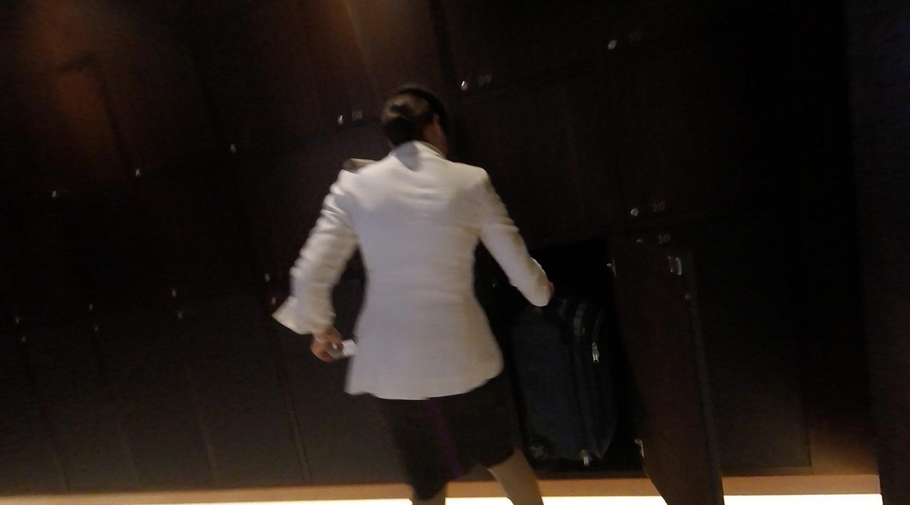 Person in a white jacket putting a blue suitcase into a dark storage compartment.