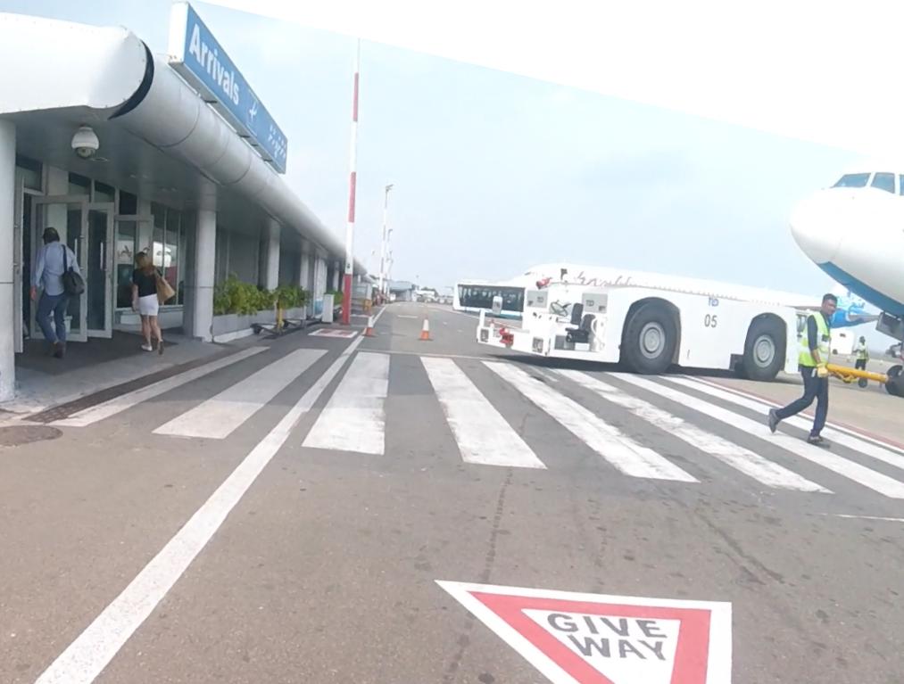 Arrivals building with passengers, an aircraft, and ground crew on the tarmac.