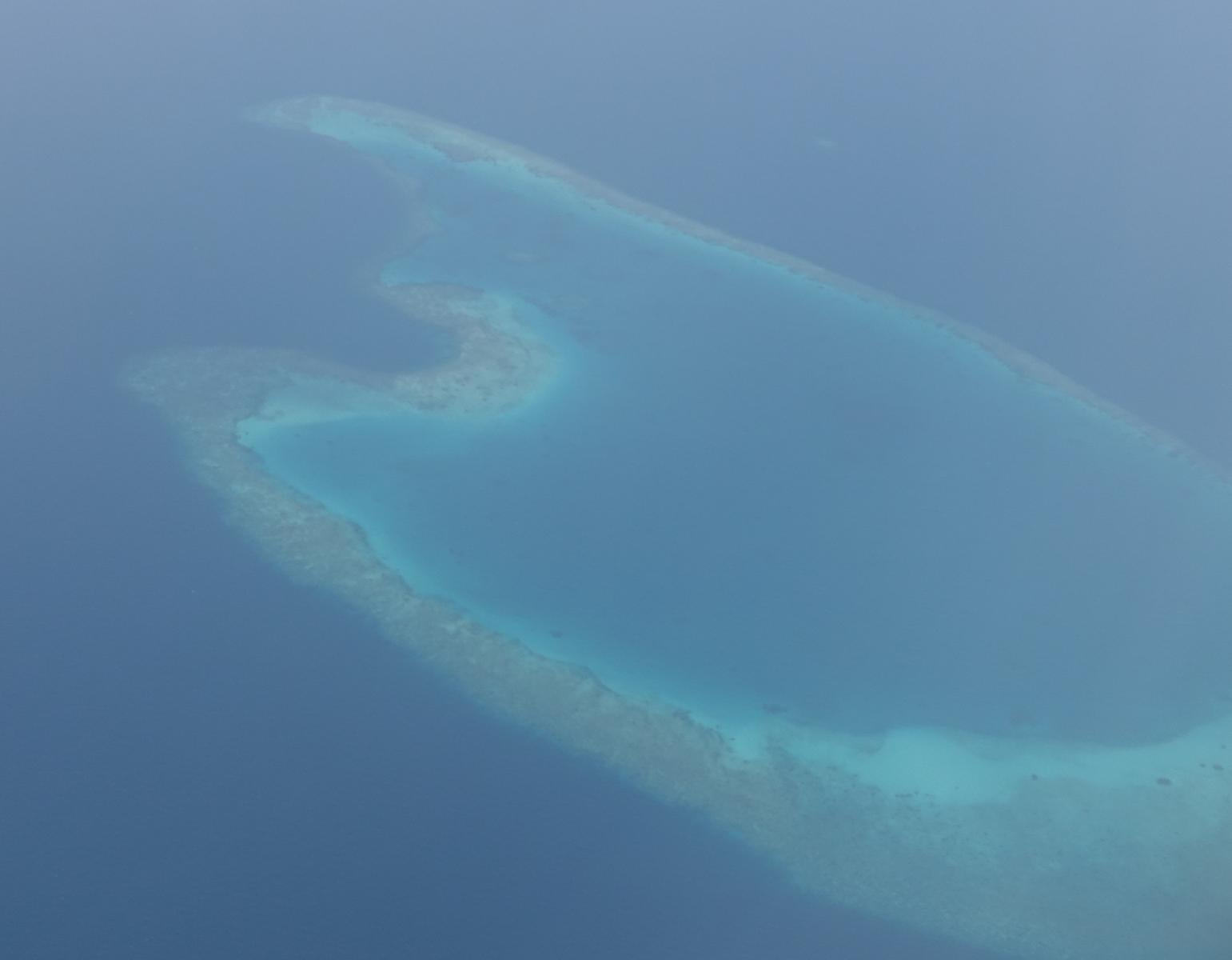 Aerial view of a shallow turquoise coral reef surrounded by deep blue ocean.