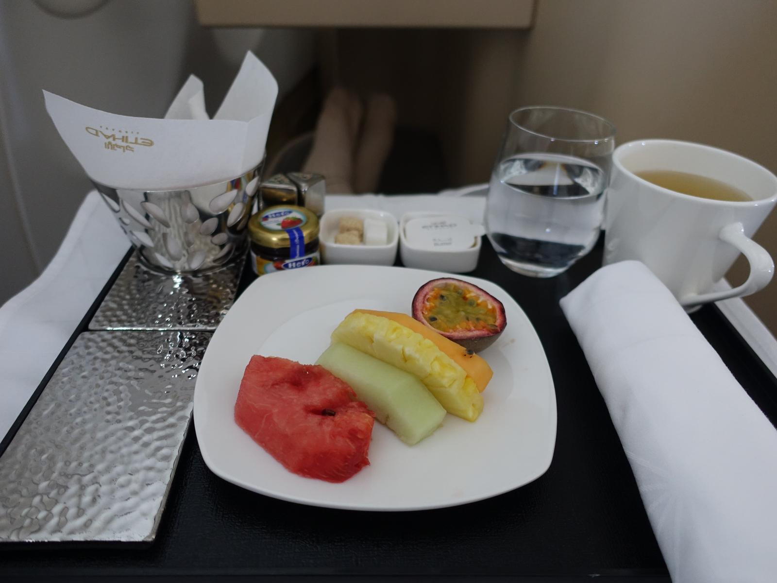 Etihad Business Class in-flight meal with a fruit plate, water, and tea.