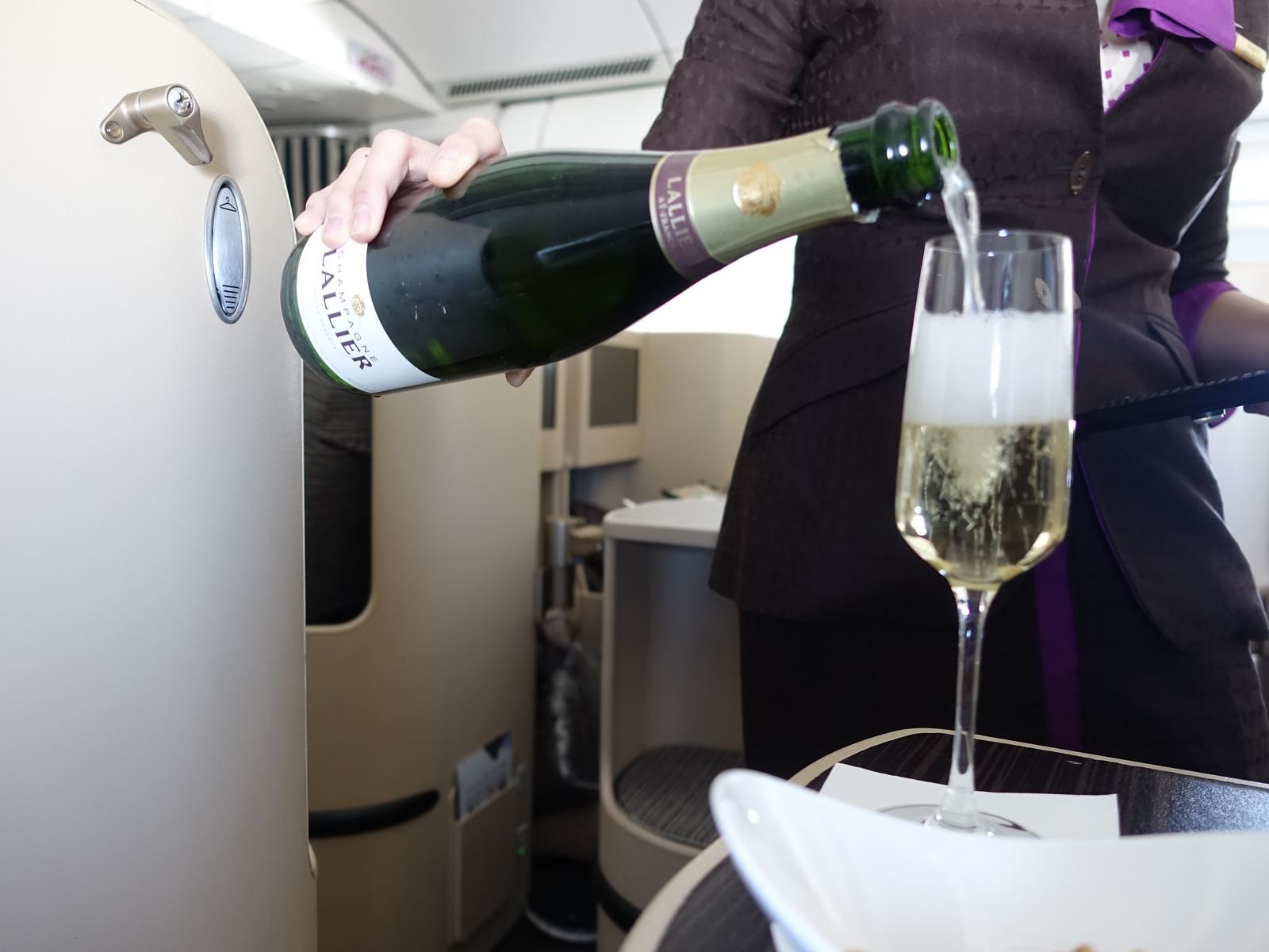 A flight attendant pours champagne into a glass in Etihad Business Class.
