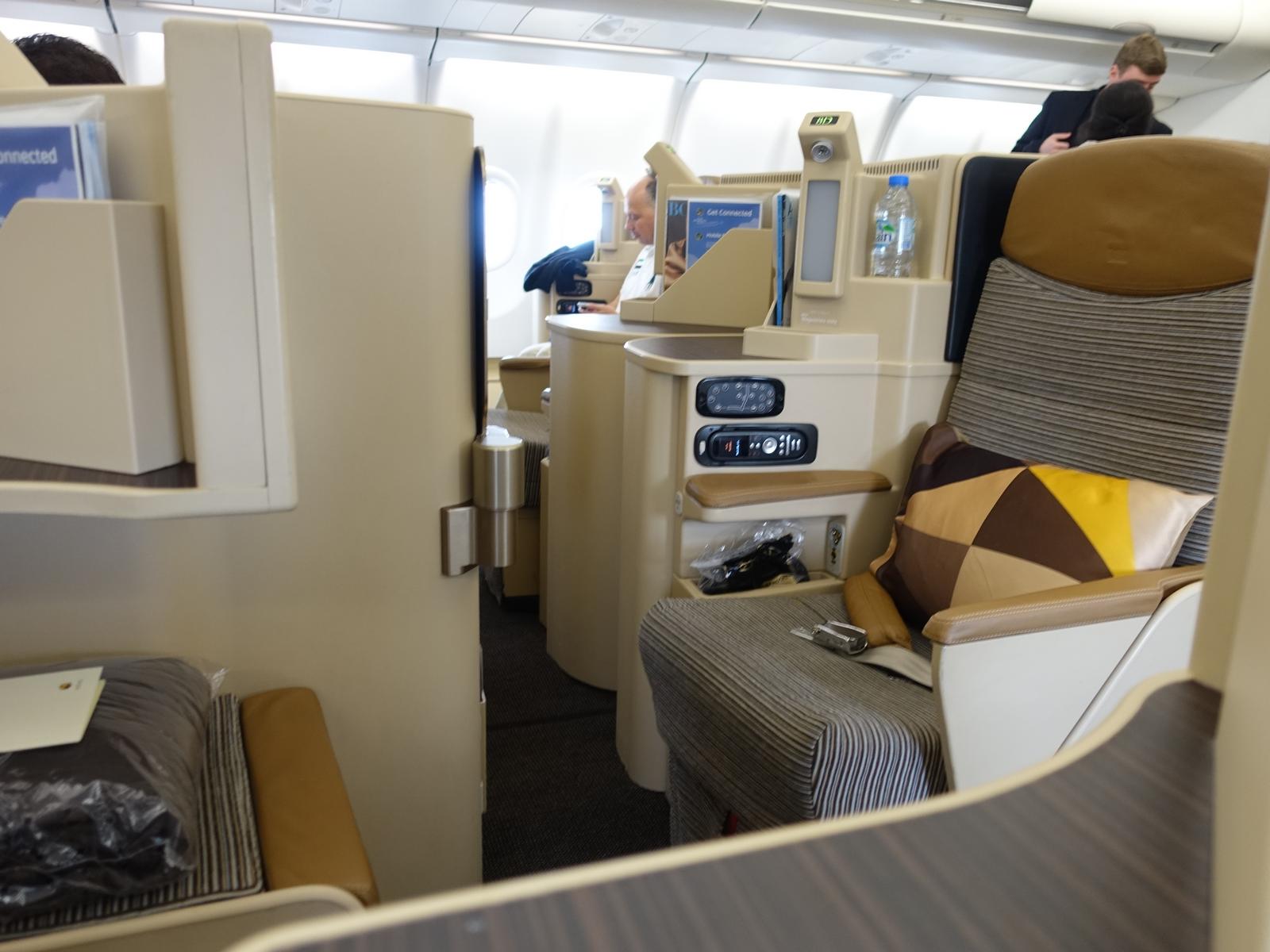 Etihad Business Class cabin with private tan and grey seating pods and amenities.