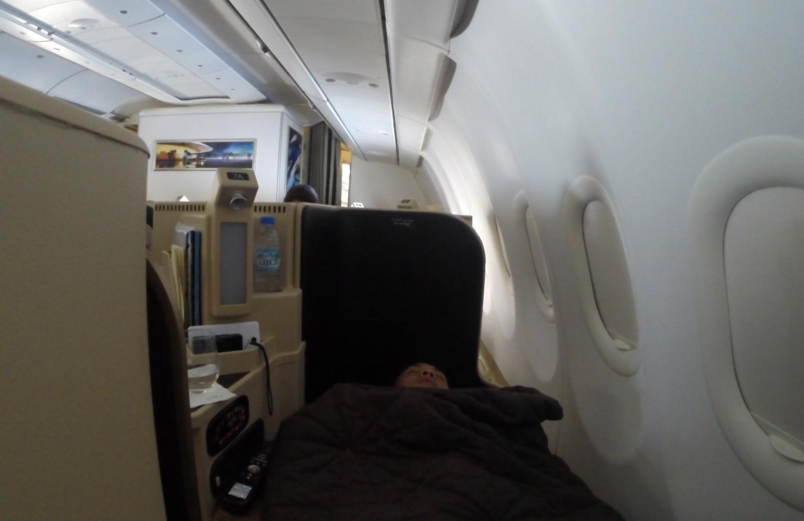 A passenger sleeps under a blanket in a flatbed window seat in Etihad Business Class.