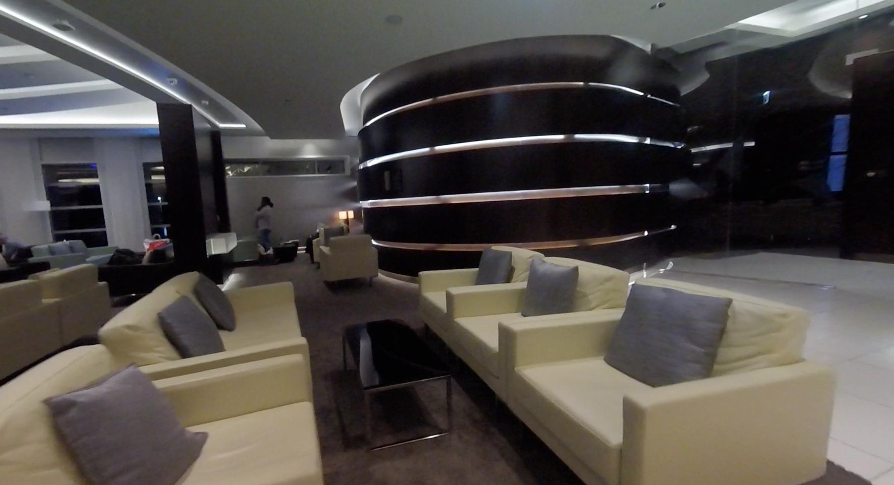 Etihad Business Class lounge with cream sofas, grey pillows, and a large dark circular illuminated feature.