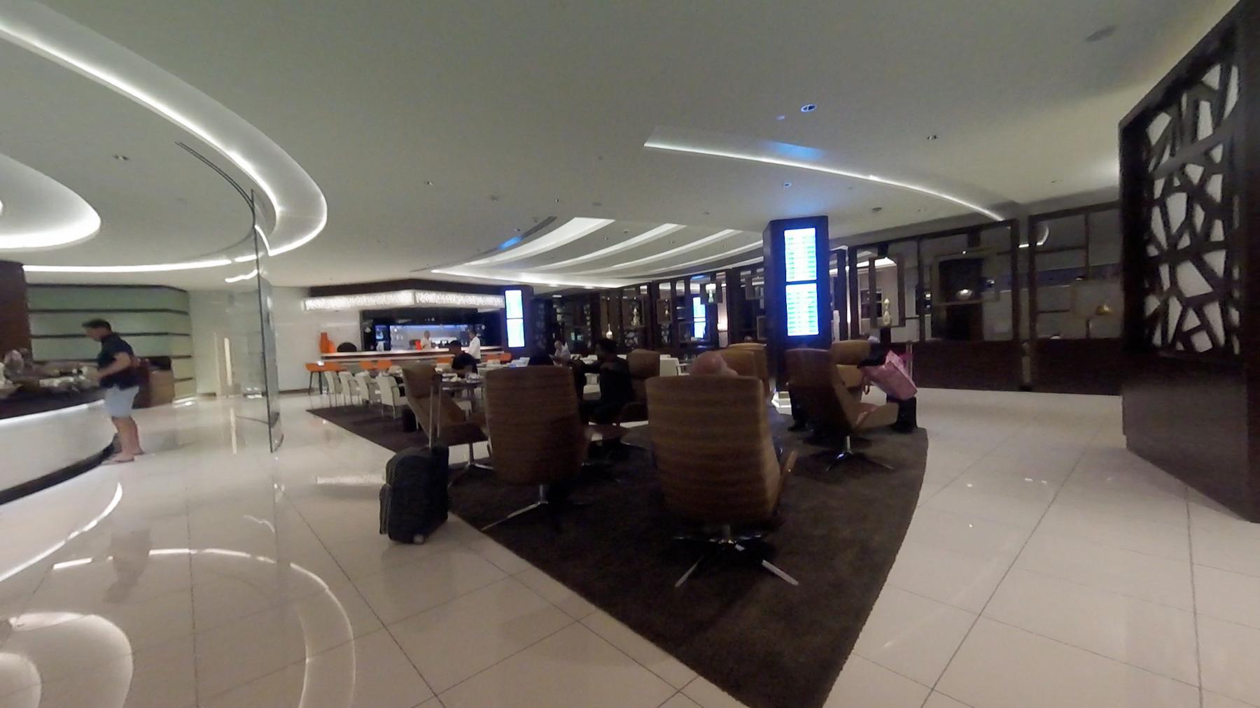 A wide interior view of the modern Etihad Business Class lounge with various seating areas and a bar.
