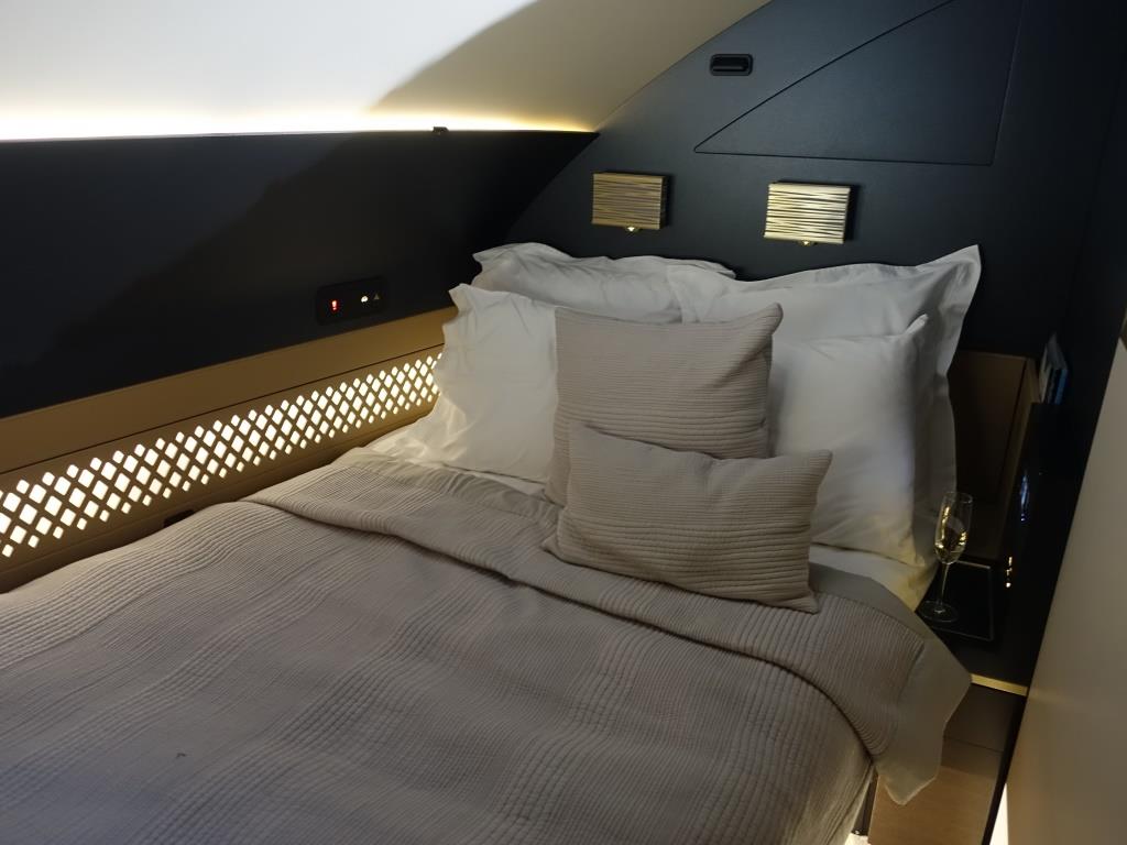 Luxurious bed in the Etihad A380 First Class cabin with ambient lighting and a champagne glass.