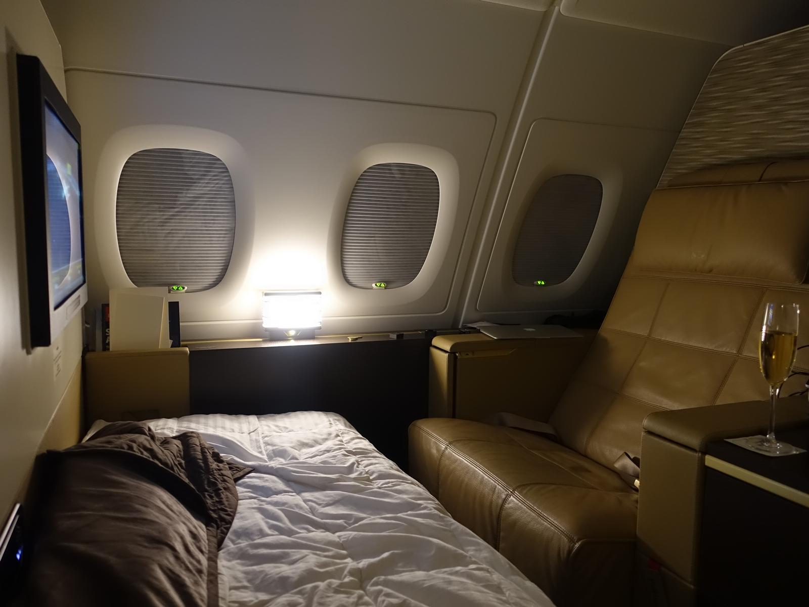 A luxurious Etihad A380 First Class apartment with a bed, armchair, and champagne.