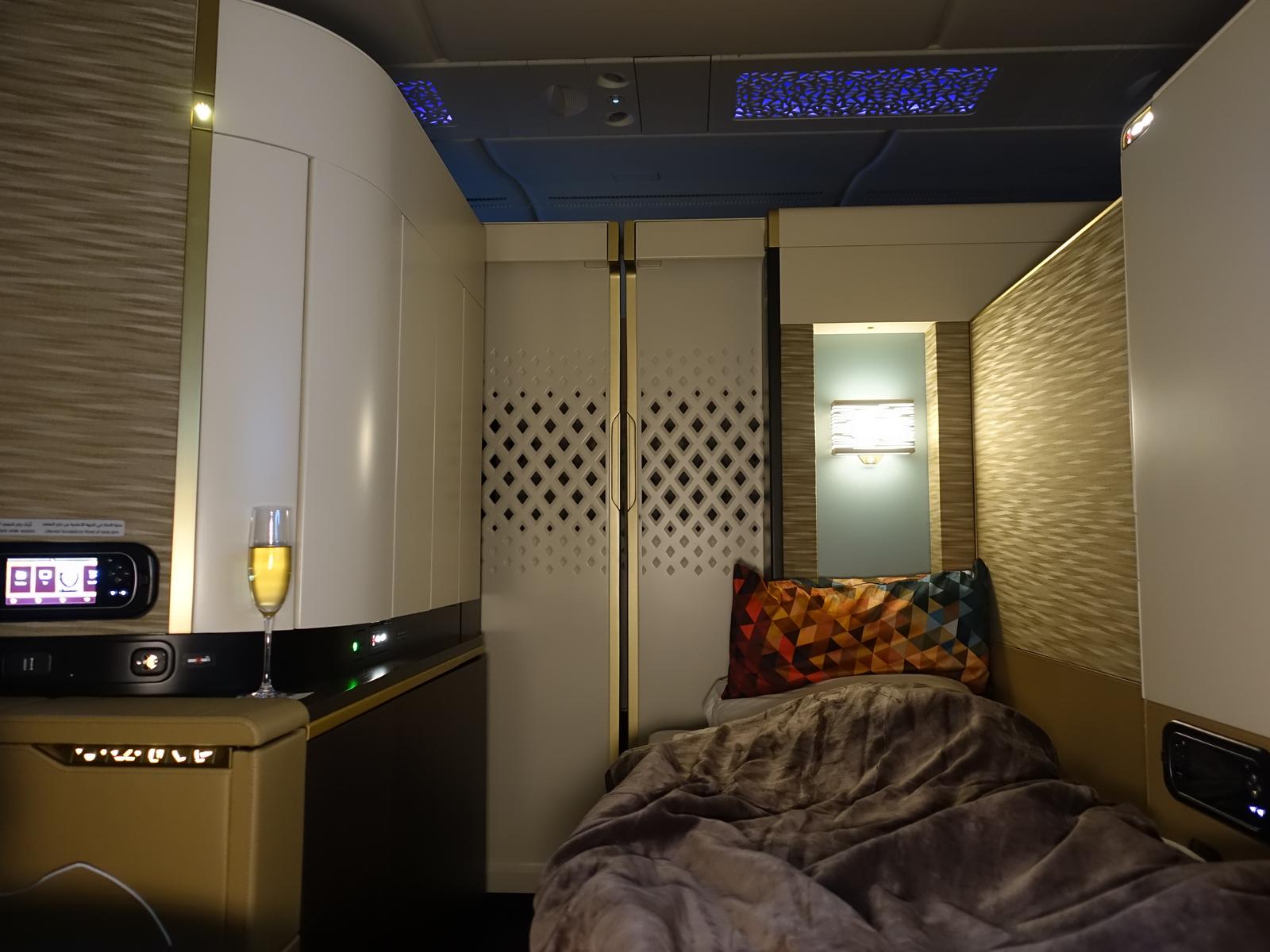 A luxurious private suite inside the Etihad A380 First Class Apartment, featuring a bed, a glass of champagne, and elegant decor.
