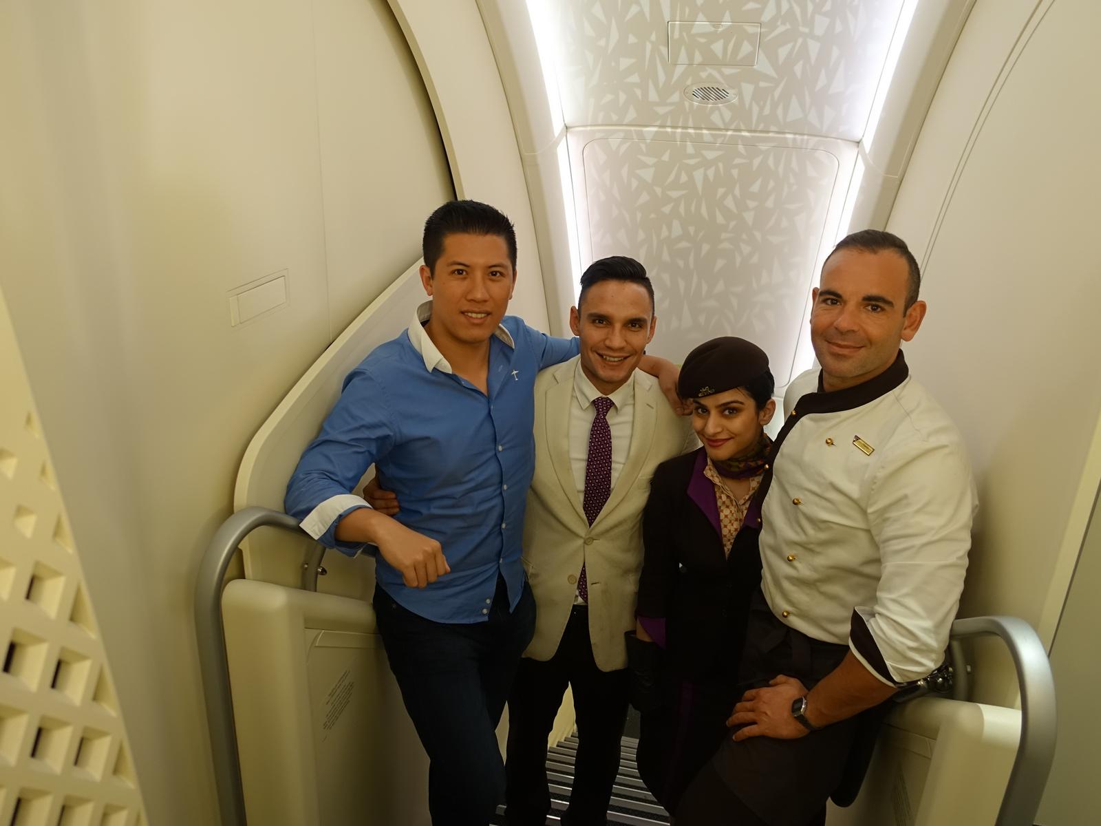 A smiling passenger poses with three Etihad Airways crew members on the A380's internal staircase.