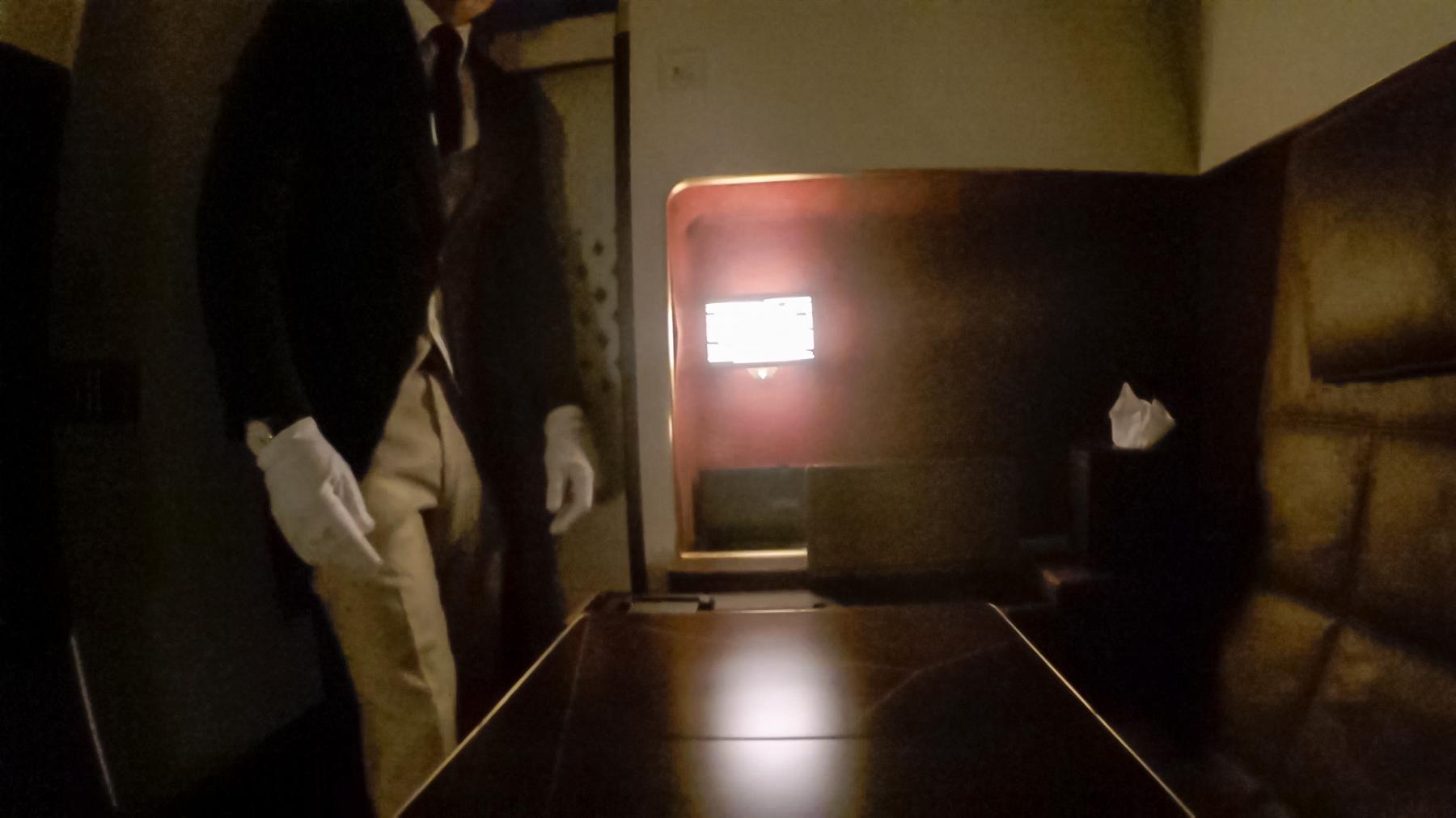 A white-gloved attendant stands in a dimly lit Etihad Residence cabin.