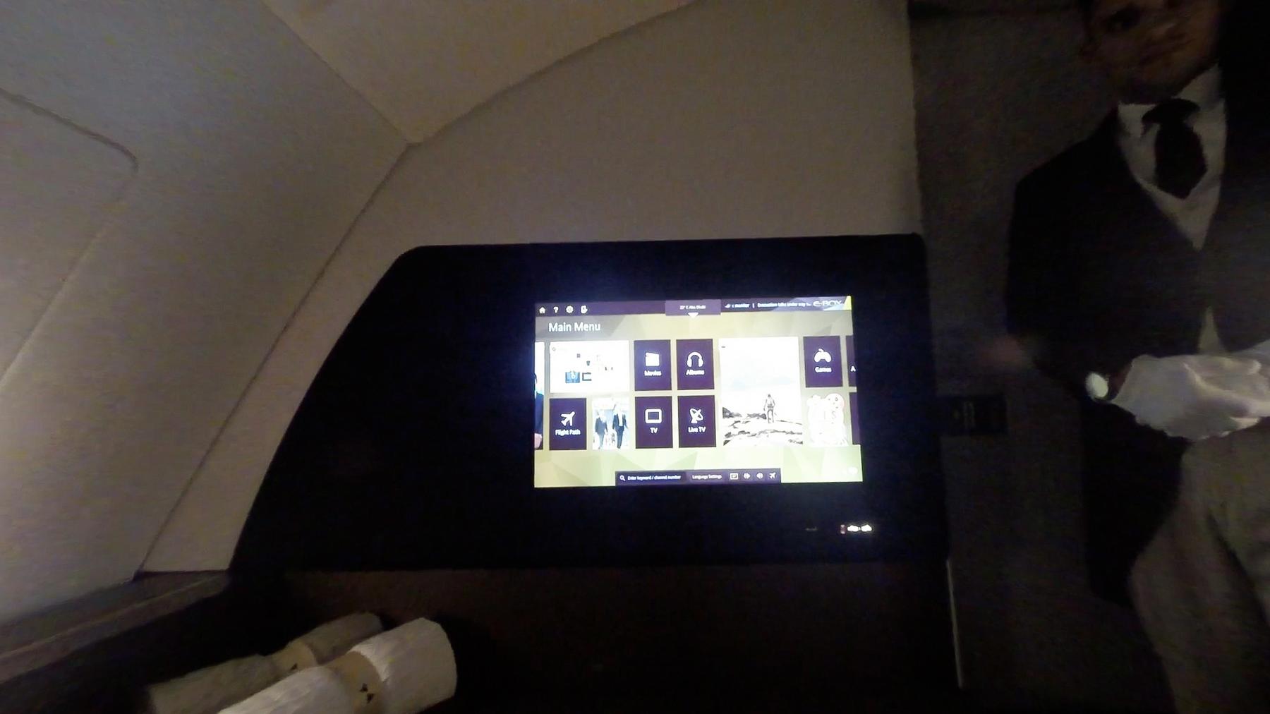 An in-flight entertainment screen displays a main menu, with a uniformed butler standing in the background of an Etihad A380 First Class cabin.