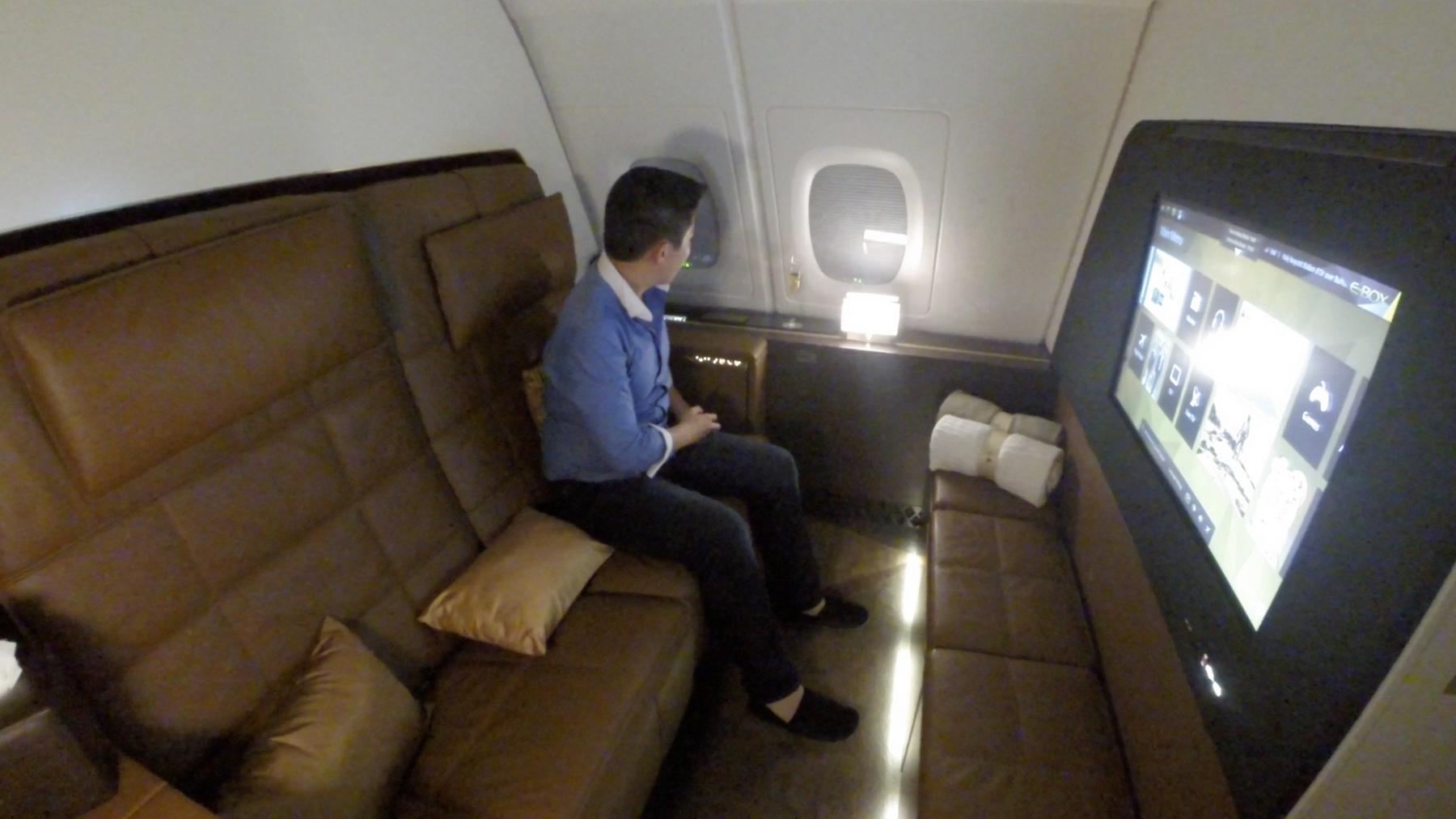 A man looks out the window of a luxurious Etihad A380 First Class apartment featuring a large entertainment screen.