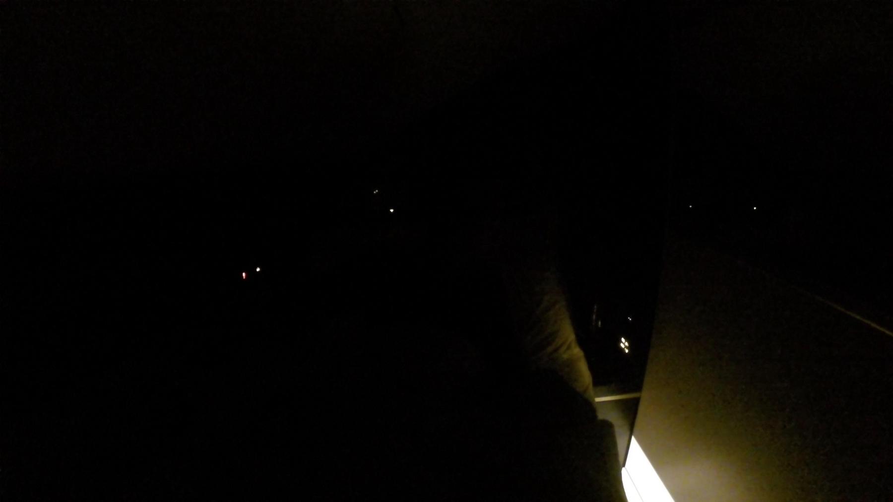 A dark night view from an airplane window with faint distant lights.