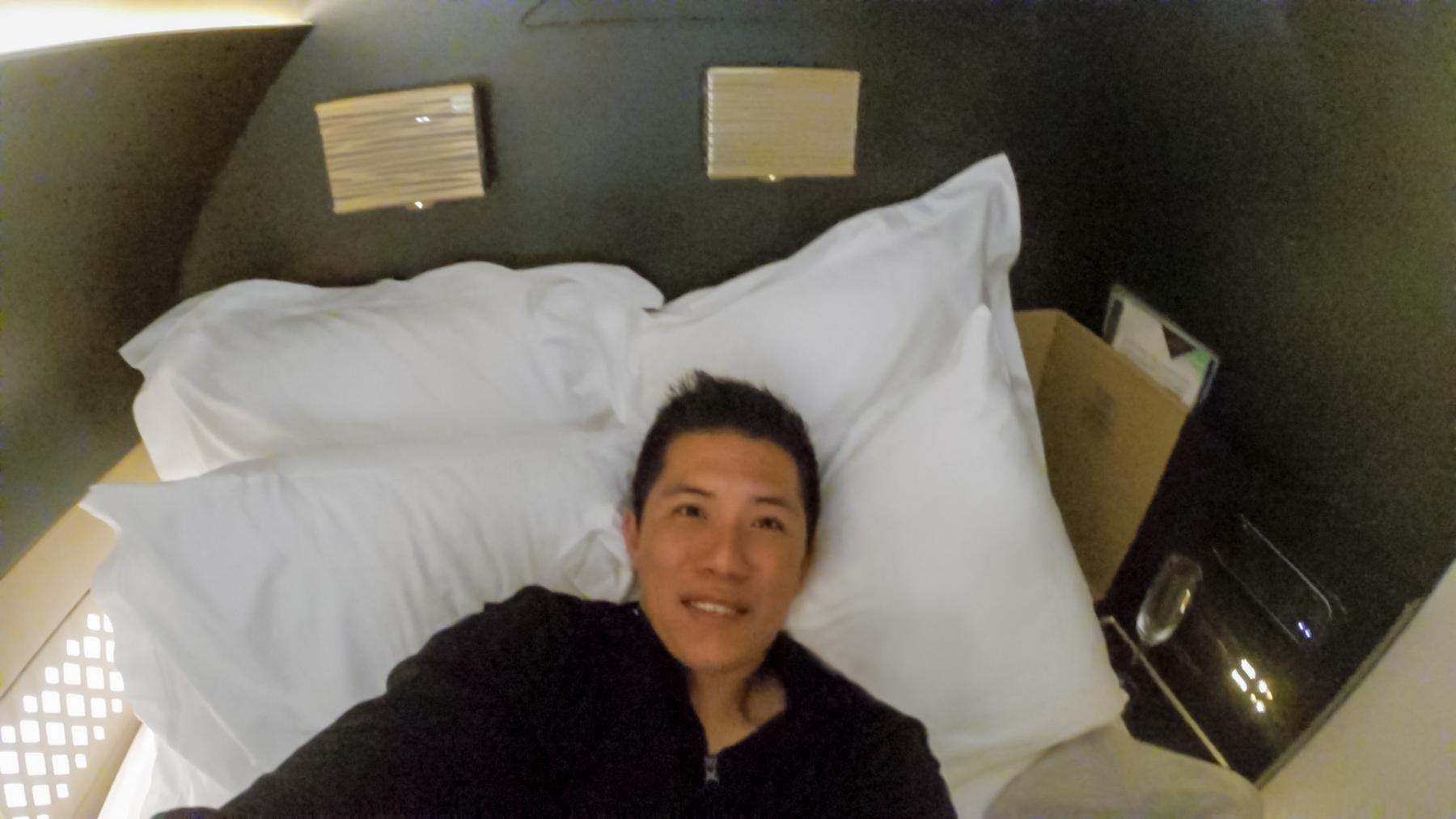 A man smiles while lying comfortably in a luxurious bed in an airline cabin.