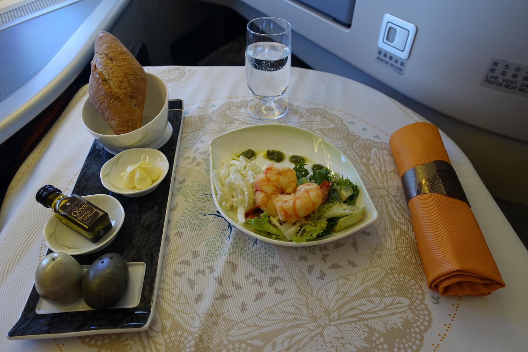 An Eva Air business class meal of shrimp salad, bread, and water on an airplane table.