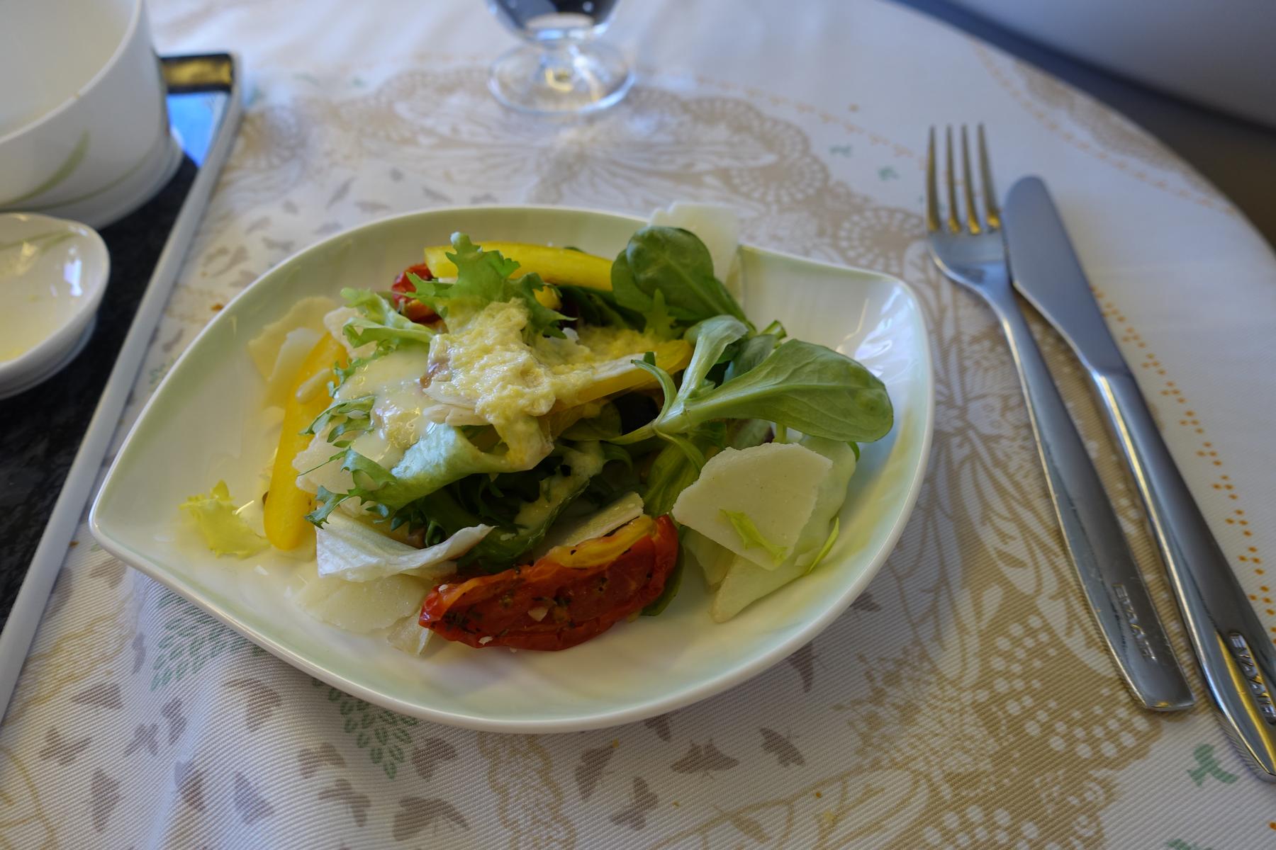 A plate of fresh salad with dressing, cutlery, and a patterned tablecloth.