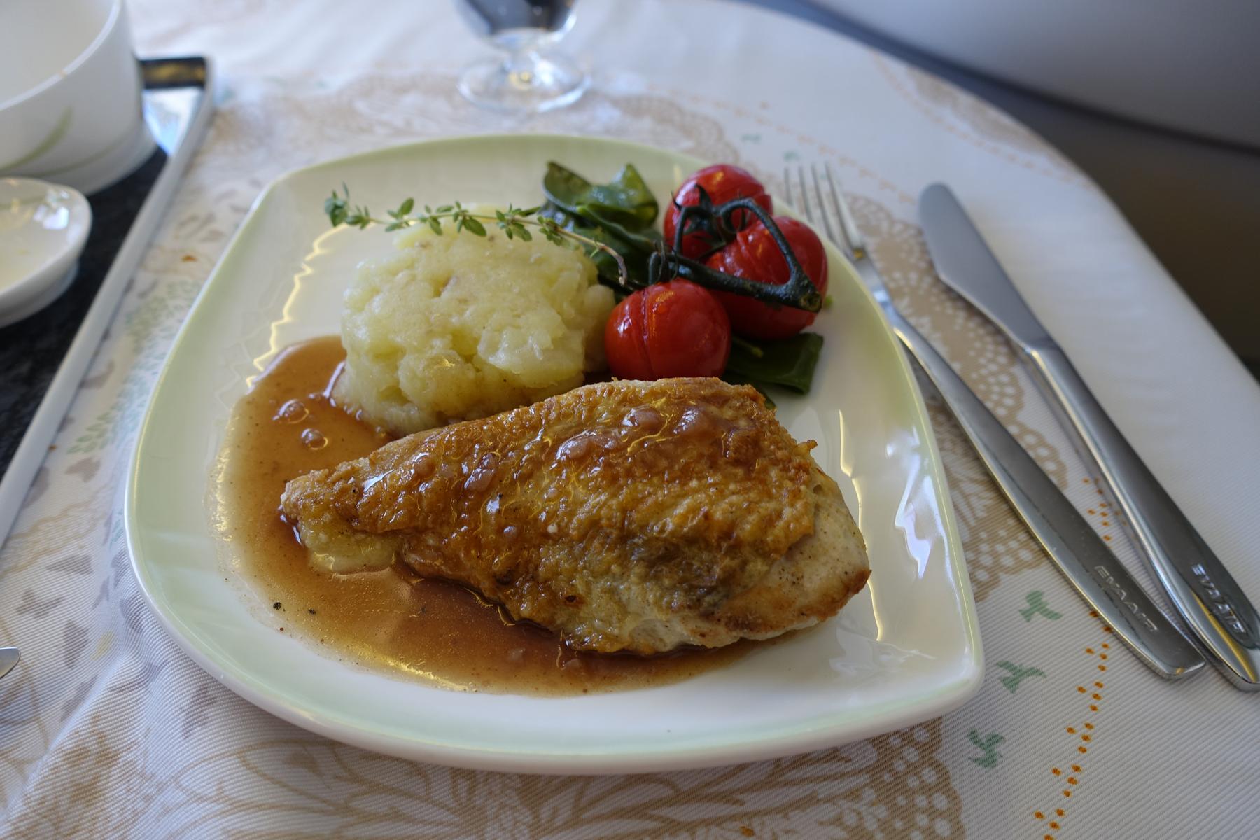 An Eva Air Business Class meal featuring a chicken breast, mashed potatoes, roasted tomatoes, and green vegetables.