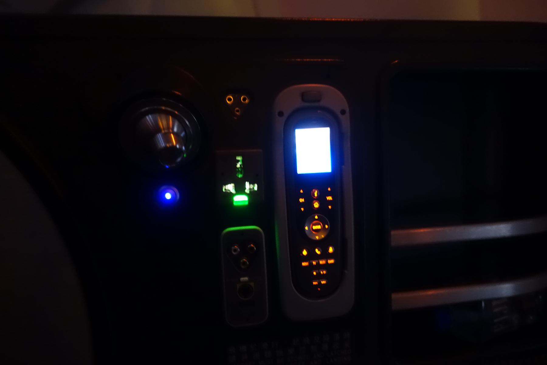 Illuminated control panel in an Eva Air Business Class seat, featuring a remote, power outlet, and audio jacks.