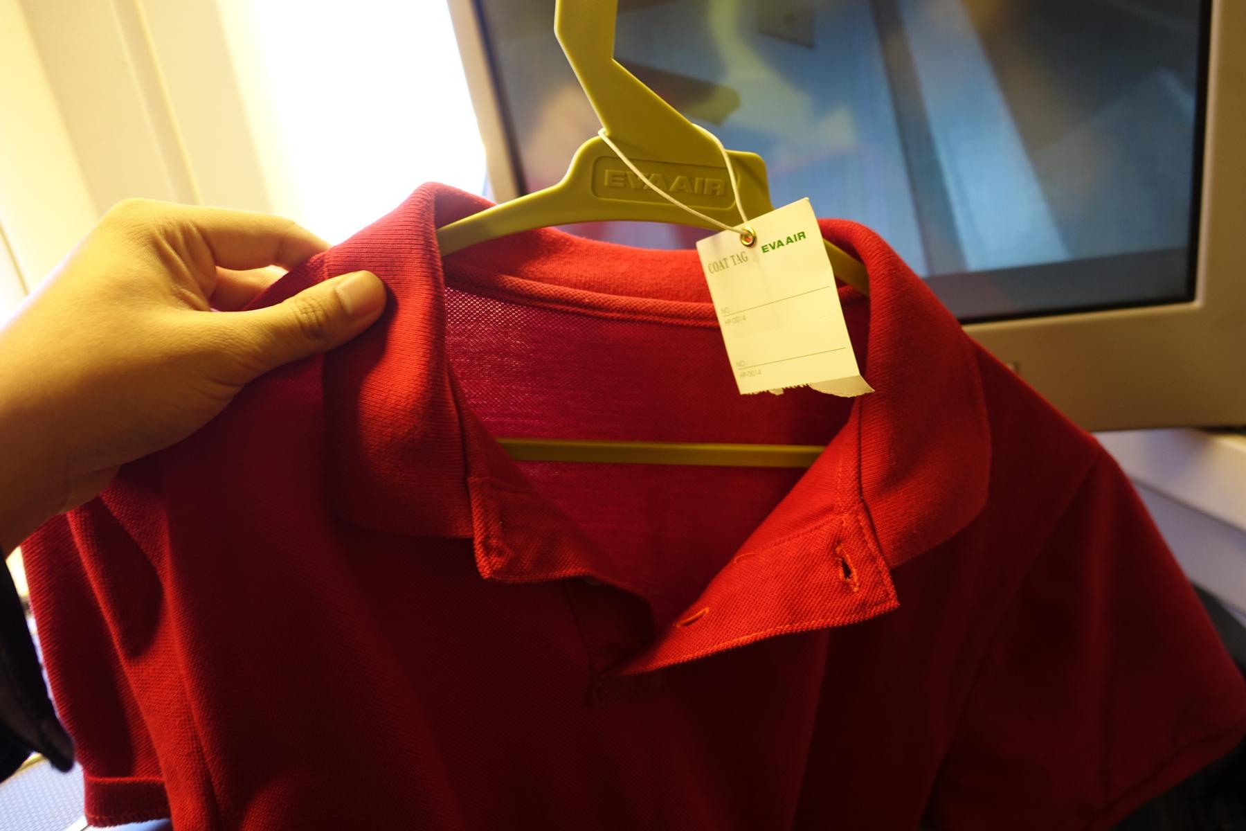 A hand holds a red polo shirt on an EVA Air branded hanger with a coat tag.