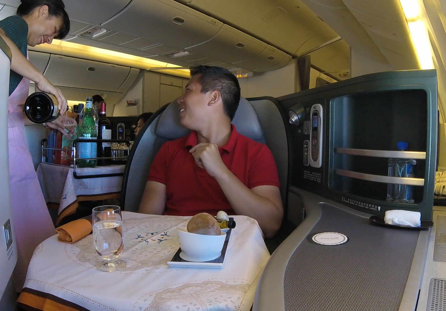 A flight attendant pours a drink for a smiling passenger in Eva Air business class.