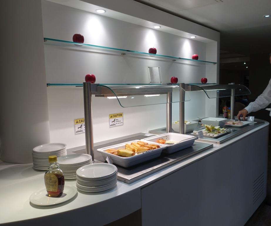 A self-service buffet counter in an airport lounge with a variety of food and a person serving themselves.
