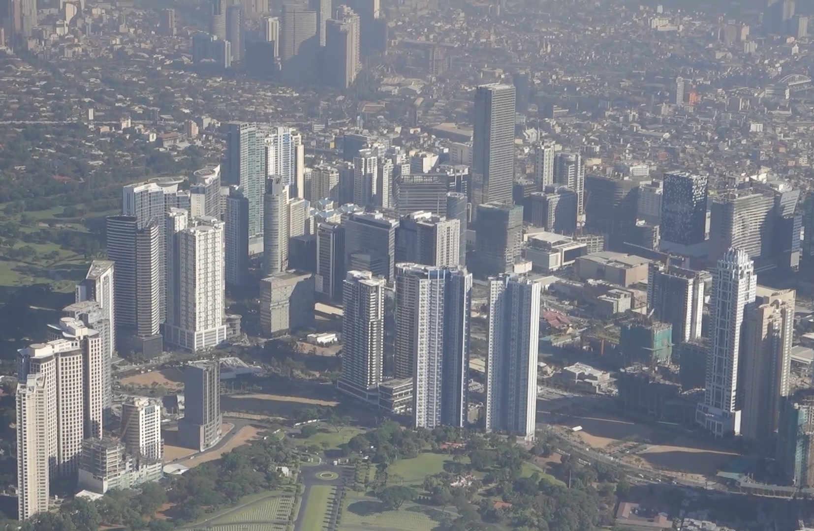 Aerial view of Manila's skyline with numerous skyscrapers and green parks.